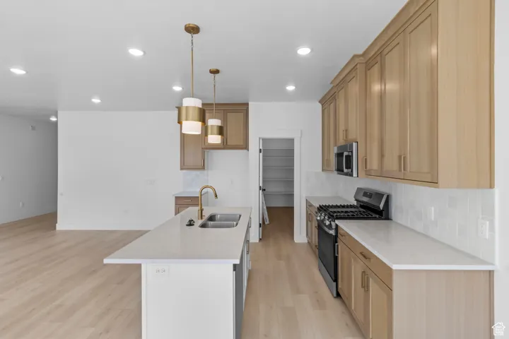 Kitchen featuring appliances with stainless steel finishes, tasteful backsplash, light wood-style flooring, pendant lighting, and light countertops