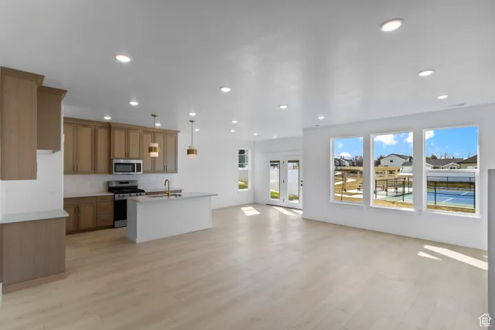 Kitchen featuring open floor plan, appliances with stainless steel finishes, a center island with sink, brown cabinetry, and light wood-type flooring
