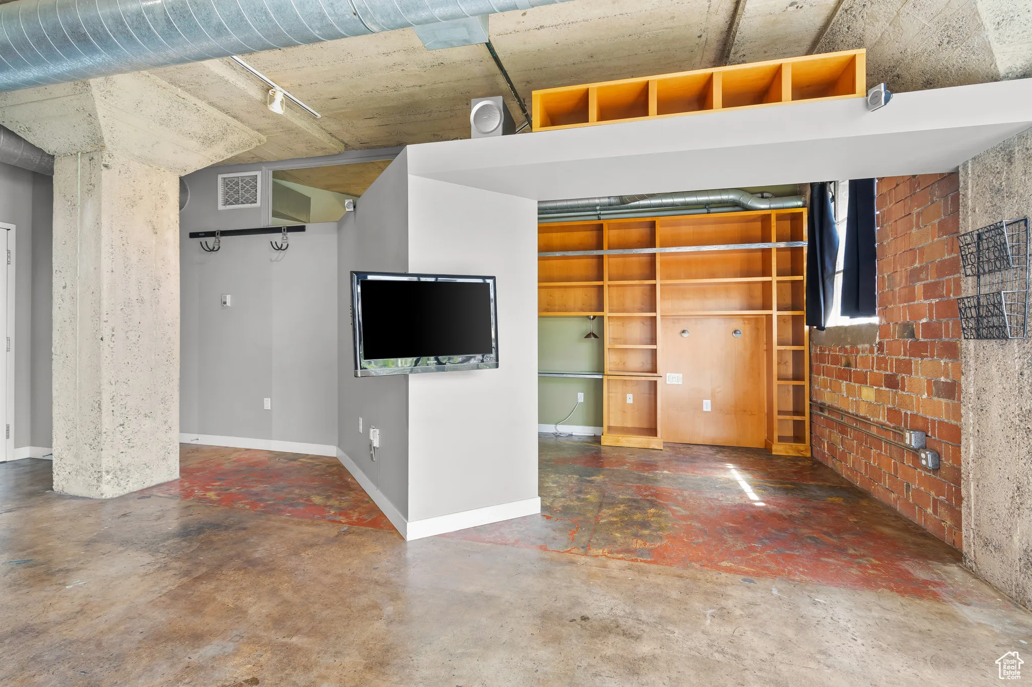Unfurnished living space featuring finished concrete floor, built in shelving, and storage.