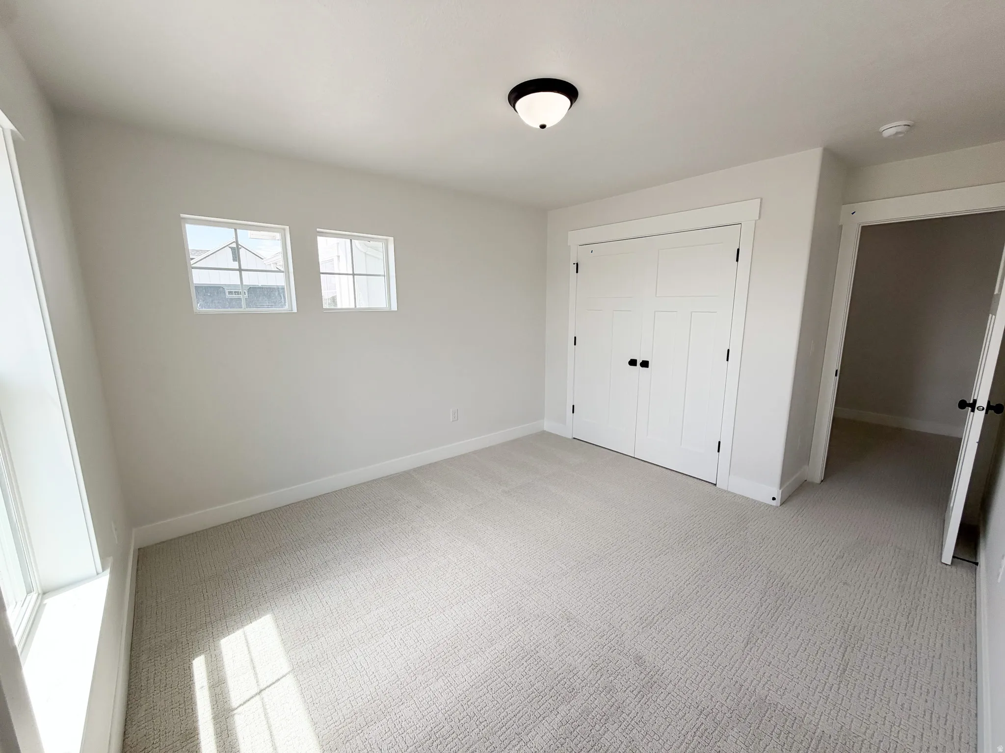 Neutral-toned bedroom featuring twin windows, light-colored carpeting, white baseboards, and a double-door closet with dark hardware