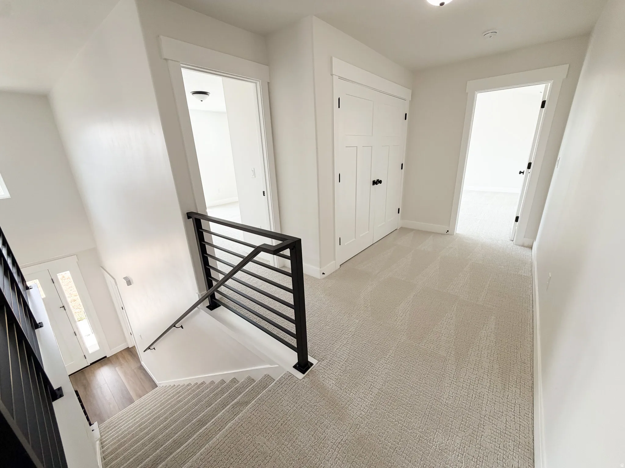 Upper-level landing featuring light-toned carpet, white walls, and a built-in closet with panel doors and black hardware