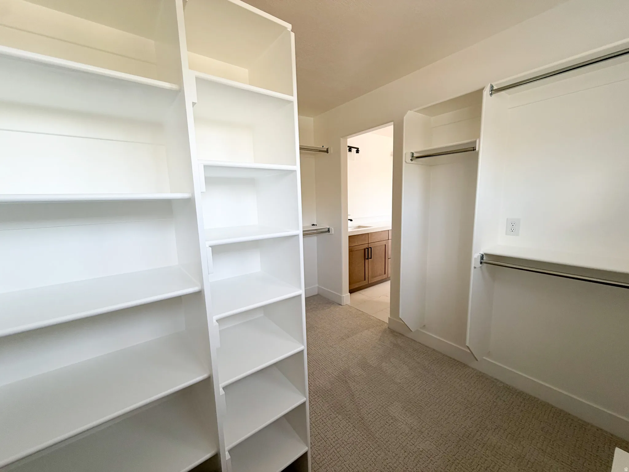 Expansive walk-in closet featuring white built-in shelving, chrome hanging rods, and neutral carpet flooring