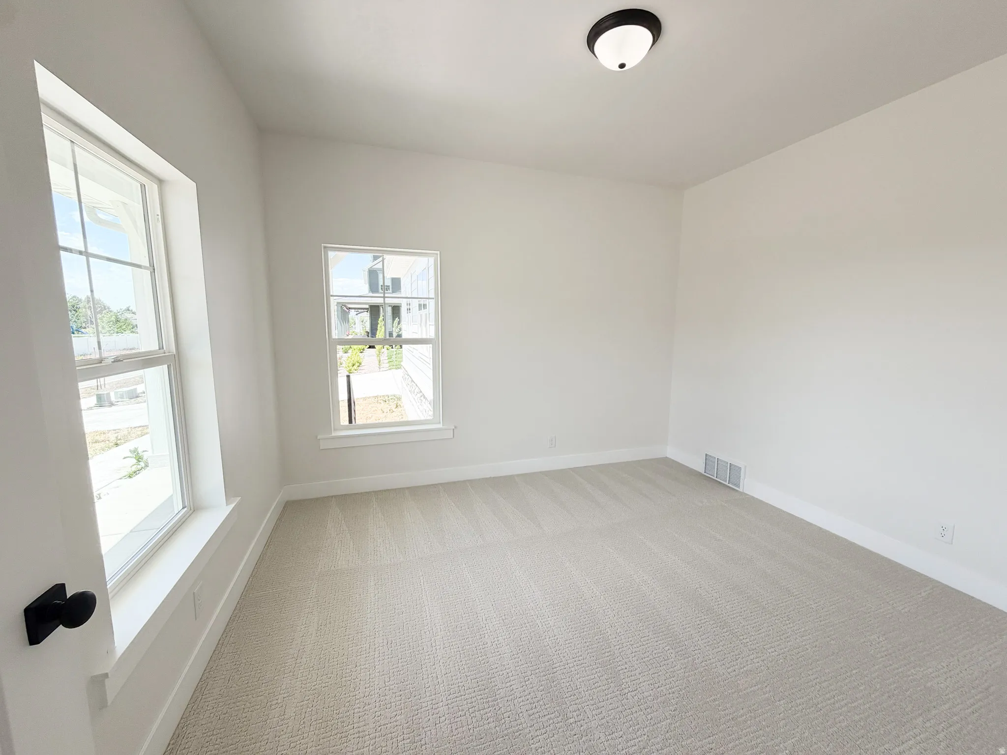 Bright interior space featuring light-toned walls, neutral patterned carpeting, and white baseboards