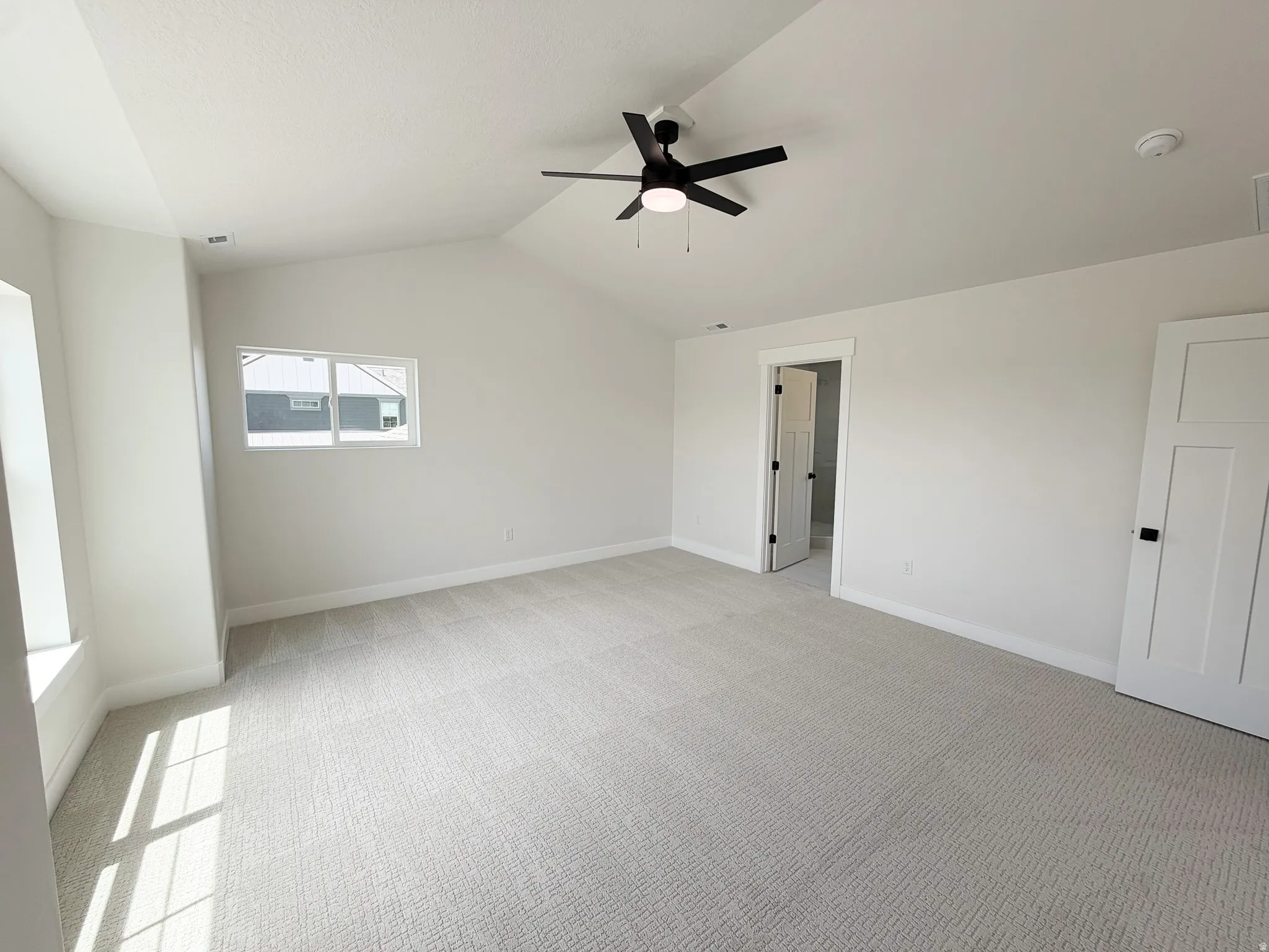 Spacious room featuring vaulted ceilings, a contemporary black ceiling fan, light gray carpeting, and multiple windows