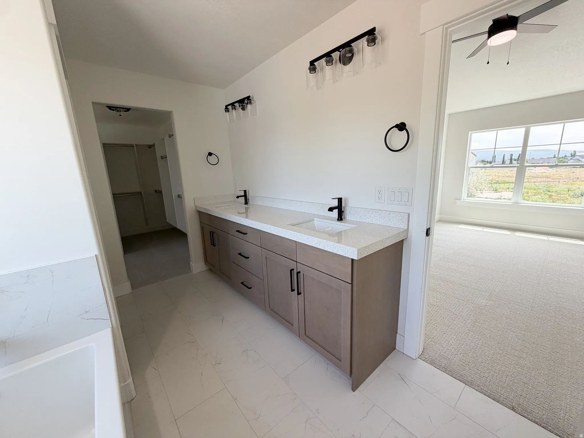 Contemporary bathroom featuring a double vanity with stone countertops and undermount sinks, matte black fixtures, modern light fixtures, and white tile flooring