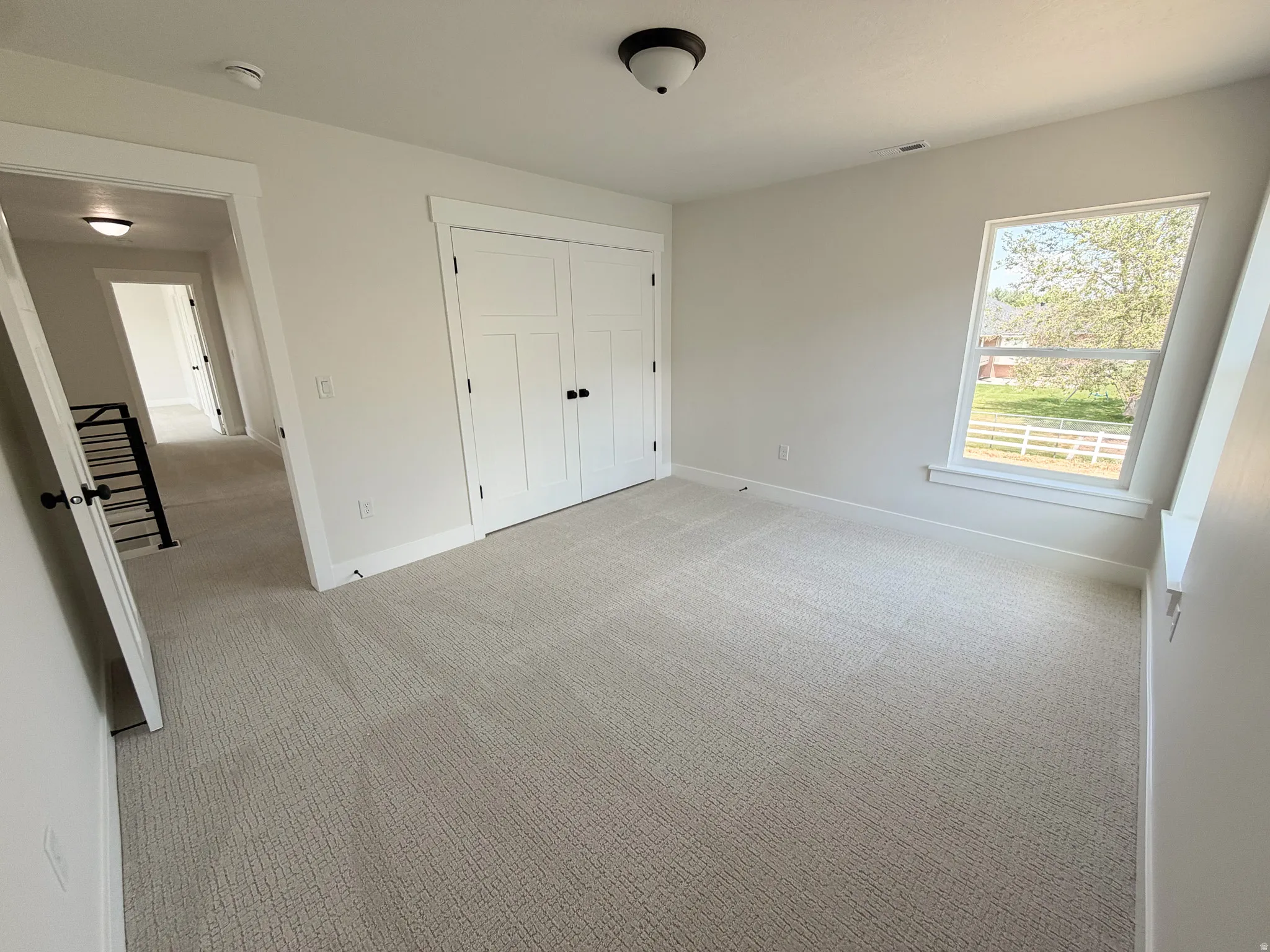 Spacious room featuring neutral carpeting, a large window, white trim, and a double-door closet with dark hardware