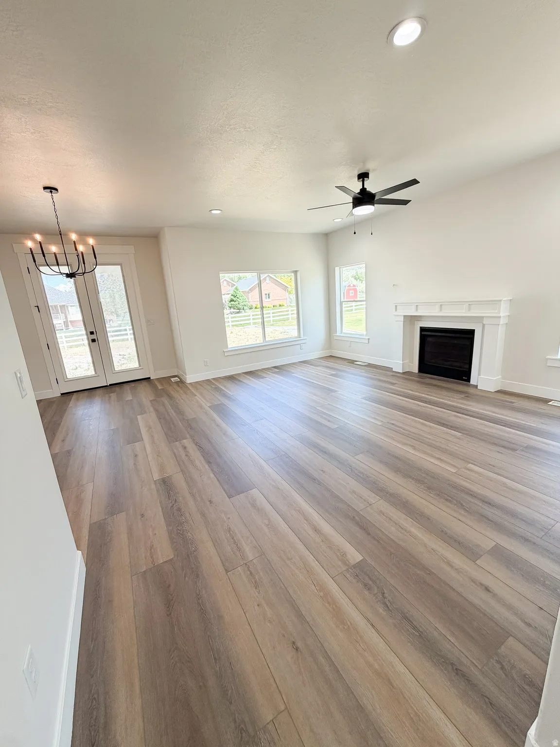 Spacious living area featuring wood-finish flooring, a fireplace with a white mantel, and vaulted ceilings with recessed lighting