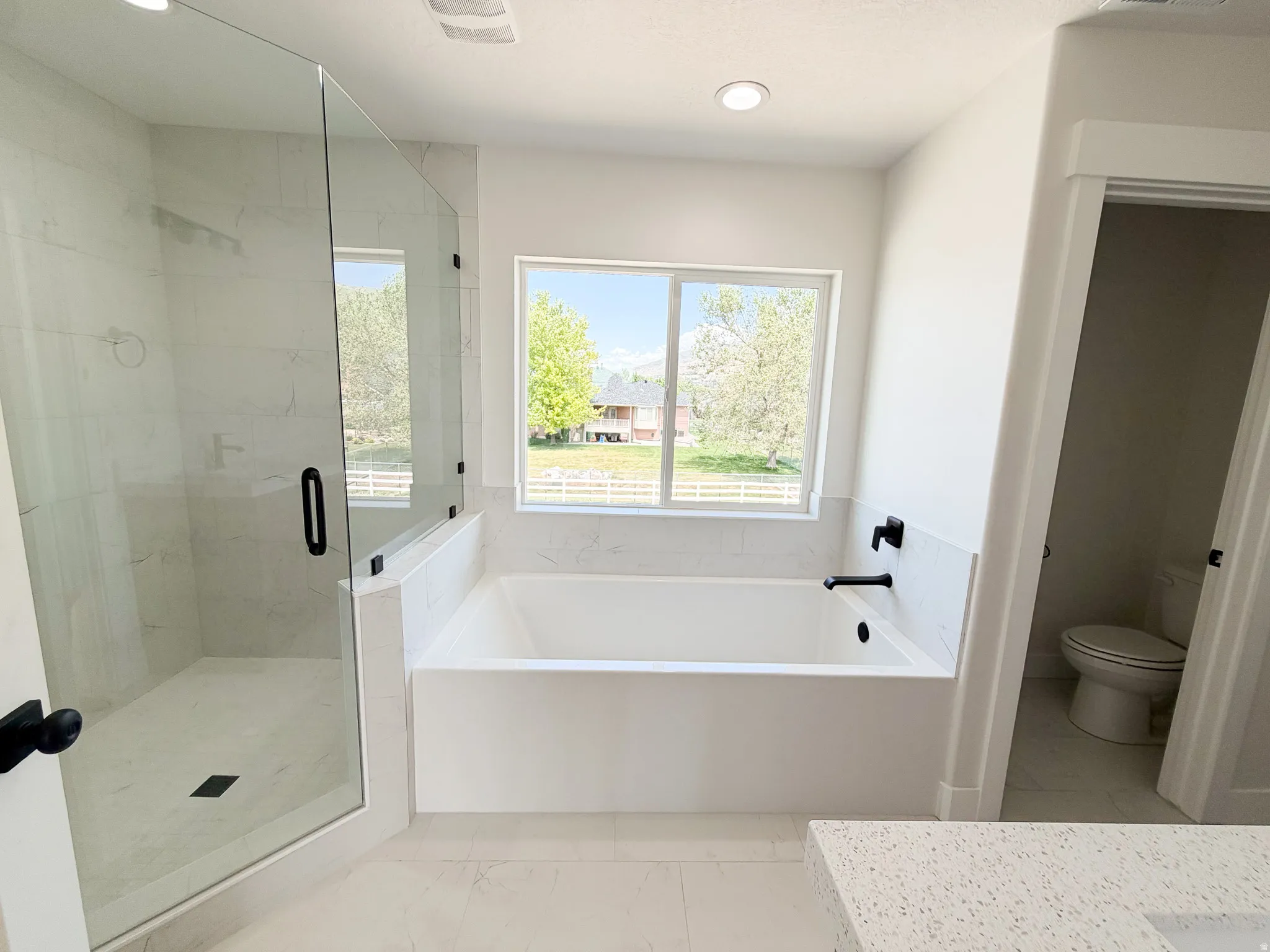 Contemporary bathroom featuring a spacious soaking tub, separate glass-enclosed shower with tile surround, and a window providing exterior views