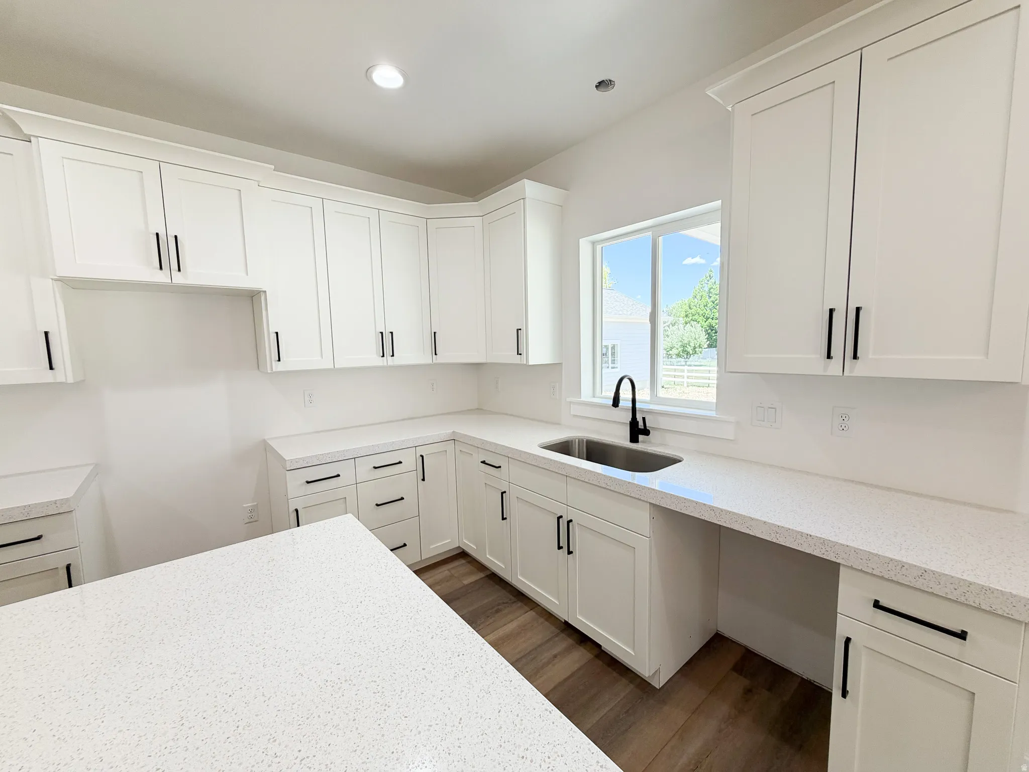 Modern kitchen featuring white shaker cabinetry with matte black hardware, speckled countertops, a stainless steel undermount sink, and wood-finish flooring
