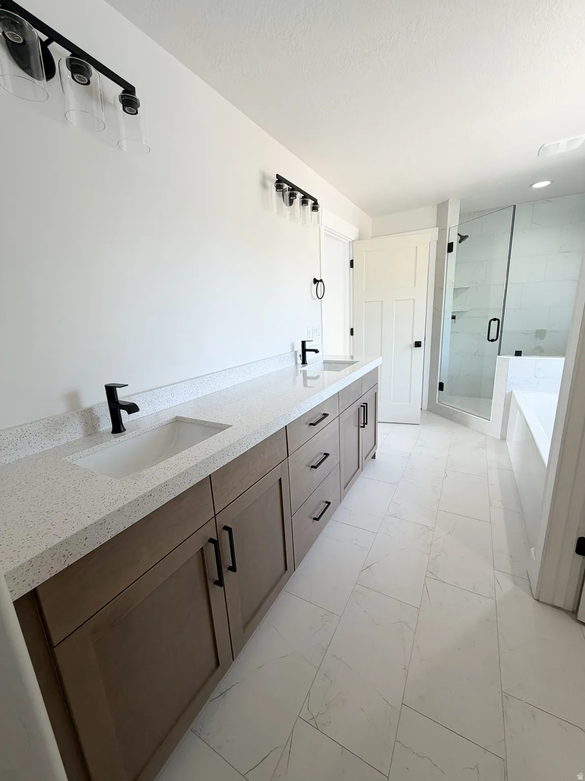 Modern bathroom featuring a dual vanity with light wood-finish cabinetry, speckled white countertops, and black fixtures