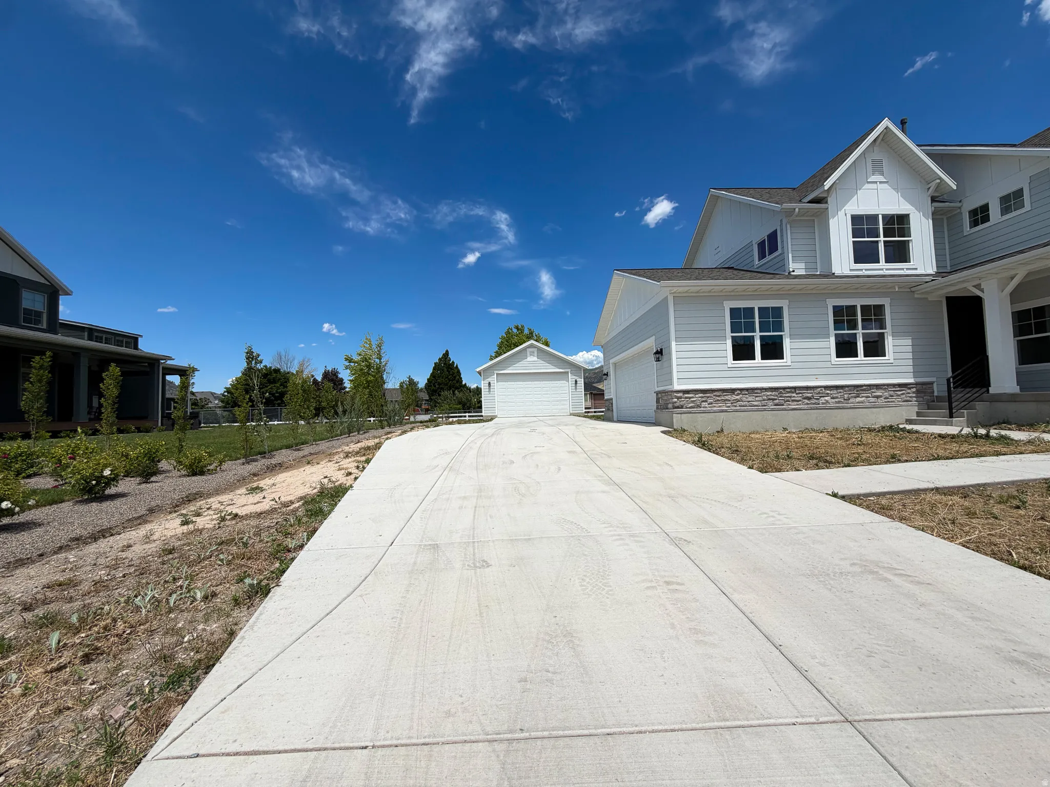 Expansive concrete driveway leading to a light-colored siding residence with a stone-finish foundation