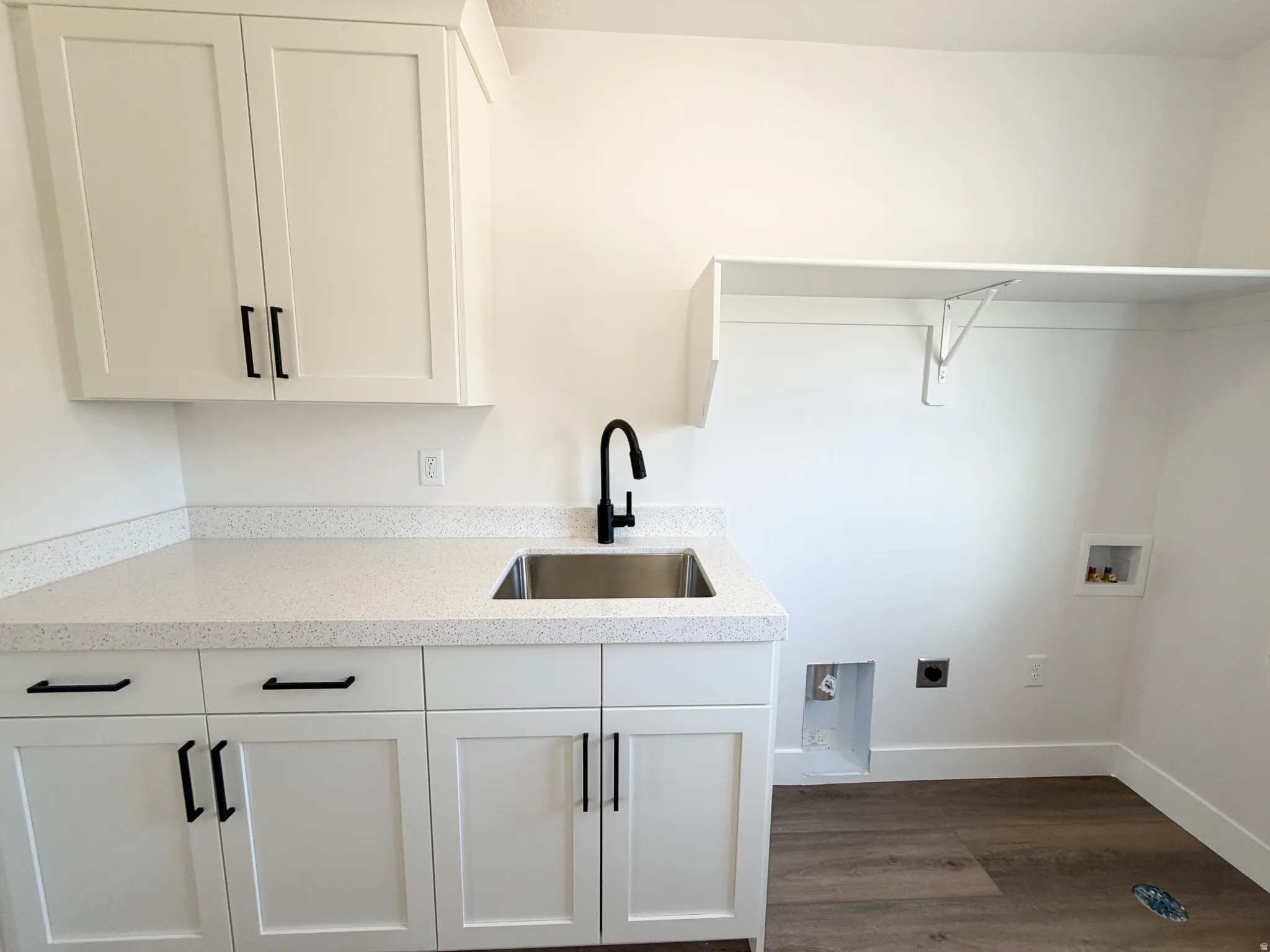 Dedicated laundry area featuring white shaker-style cabinetry, a speckled countertop, and a stainless steel utility sink with a matte black faucet
