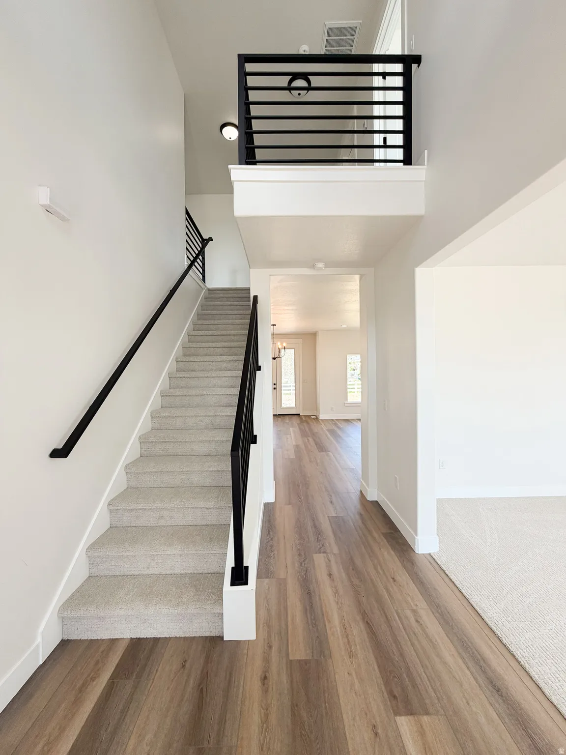 Two-story entry foyer featuring wood-finish flooring, a carpeted staircase with contemporary black metal railings, and a second-story landing with matching railings