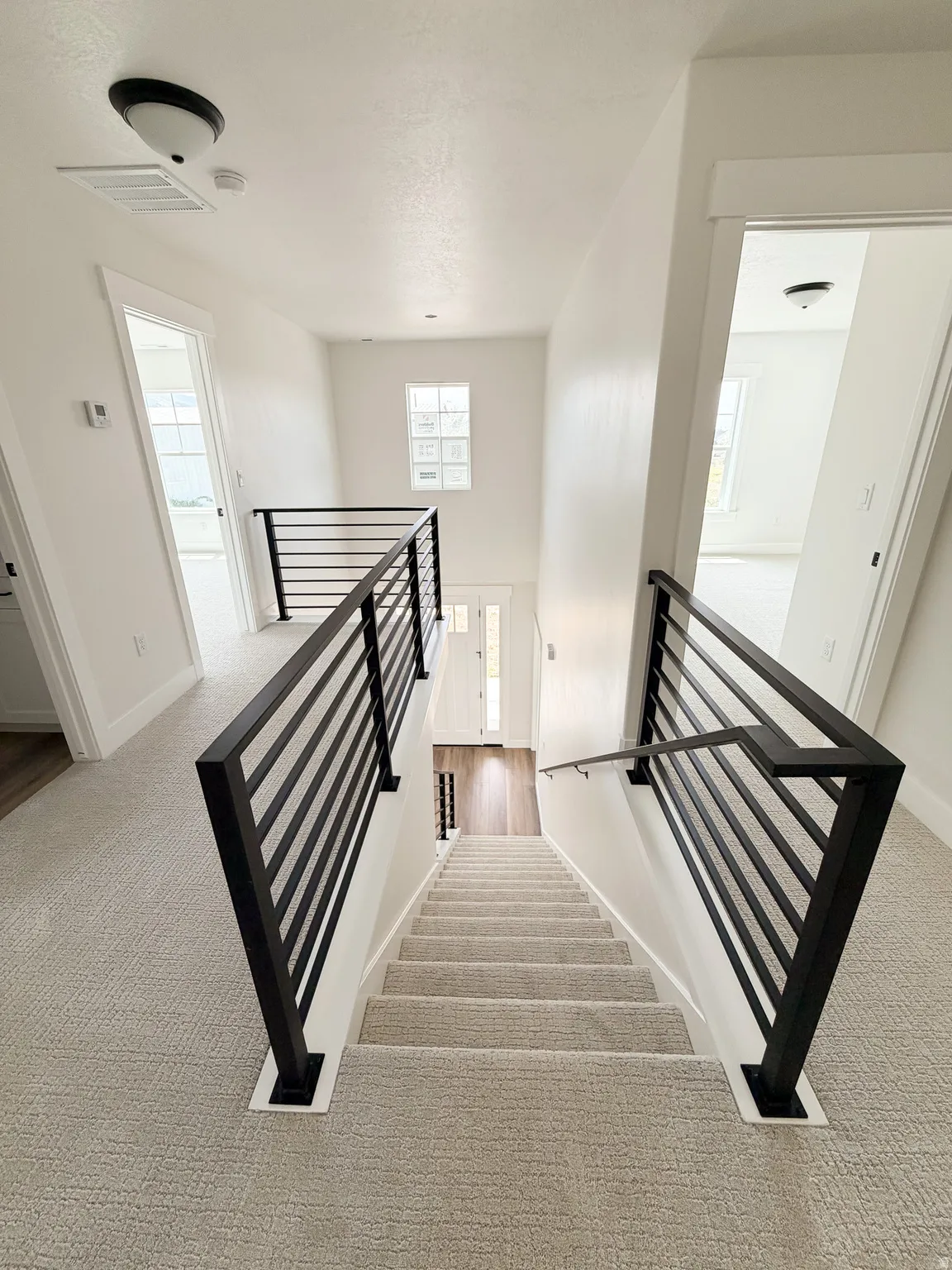 Staircase featuring modern black metal railings, light-toned carpeted treads, and wood-finish flooring at the bottom landing