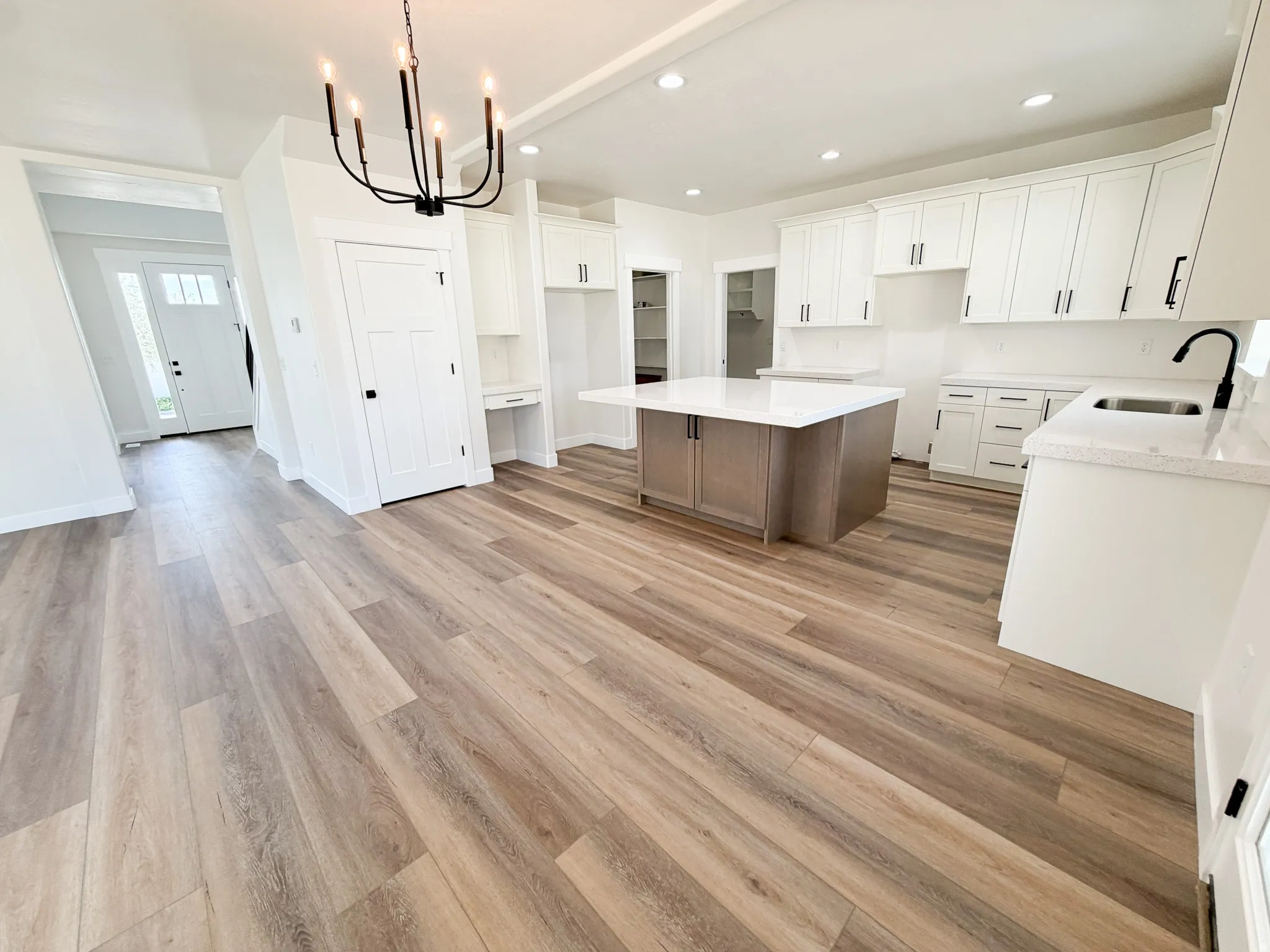 Modern kitchen featuring white cabinetry, light countertops, a central island, wood-finish flooring, and a contemporary chandelier