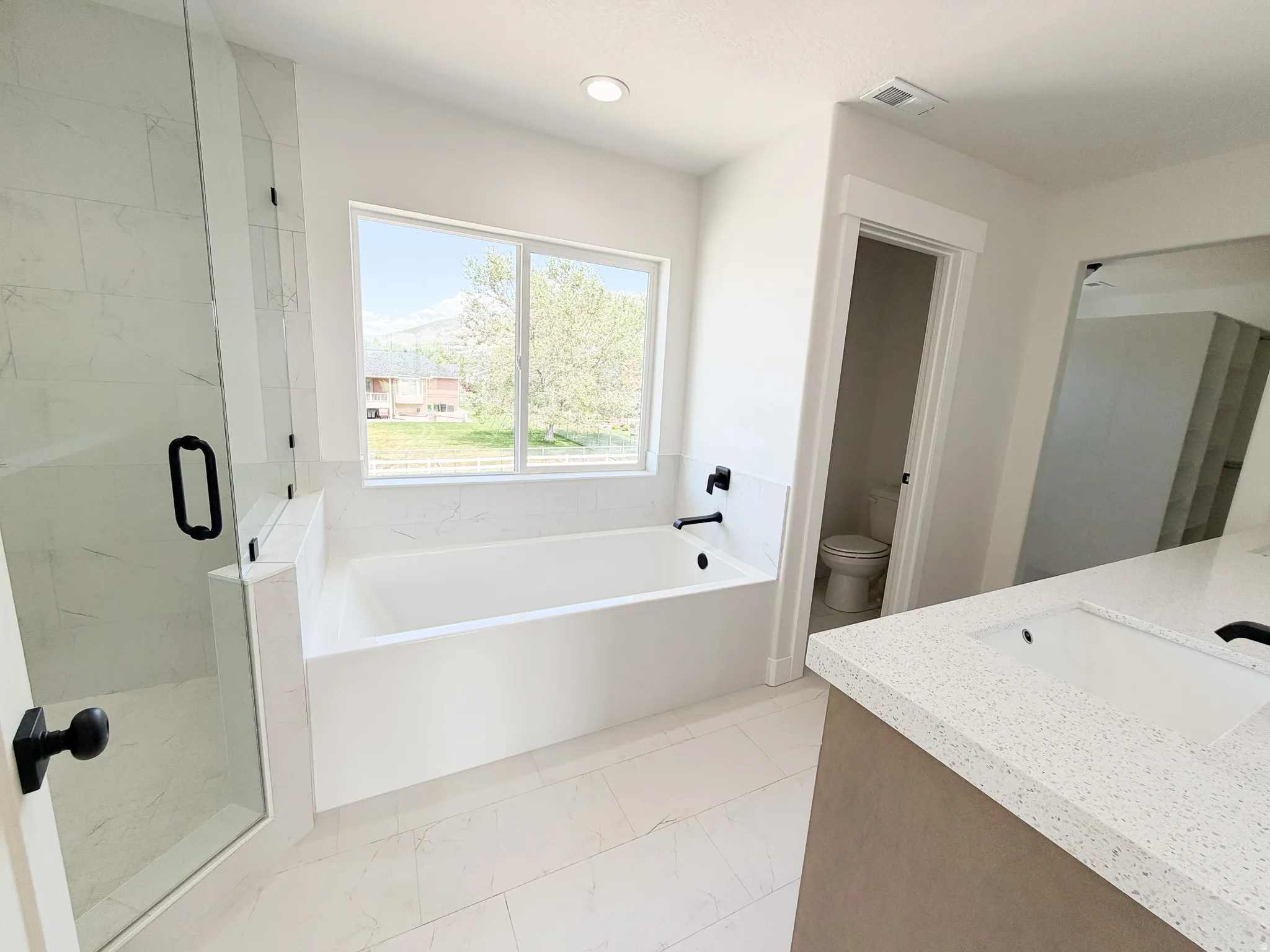Soaking tub with black fixtures, framed window, and tiled surround