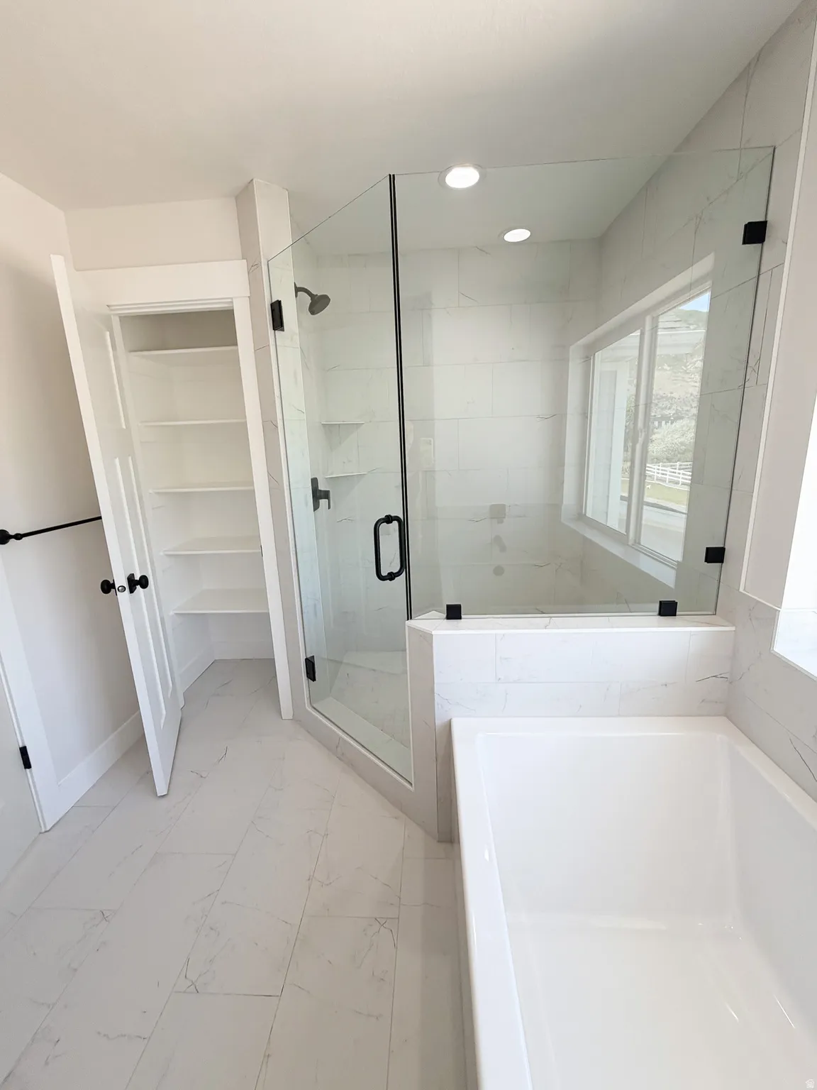 Contemporary bathroom featuring a frameless glass shower enclosure with matte black hardware, a built-in soaking tub, and a spacious linen closet with shelving