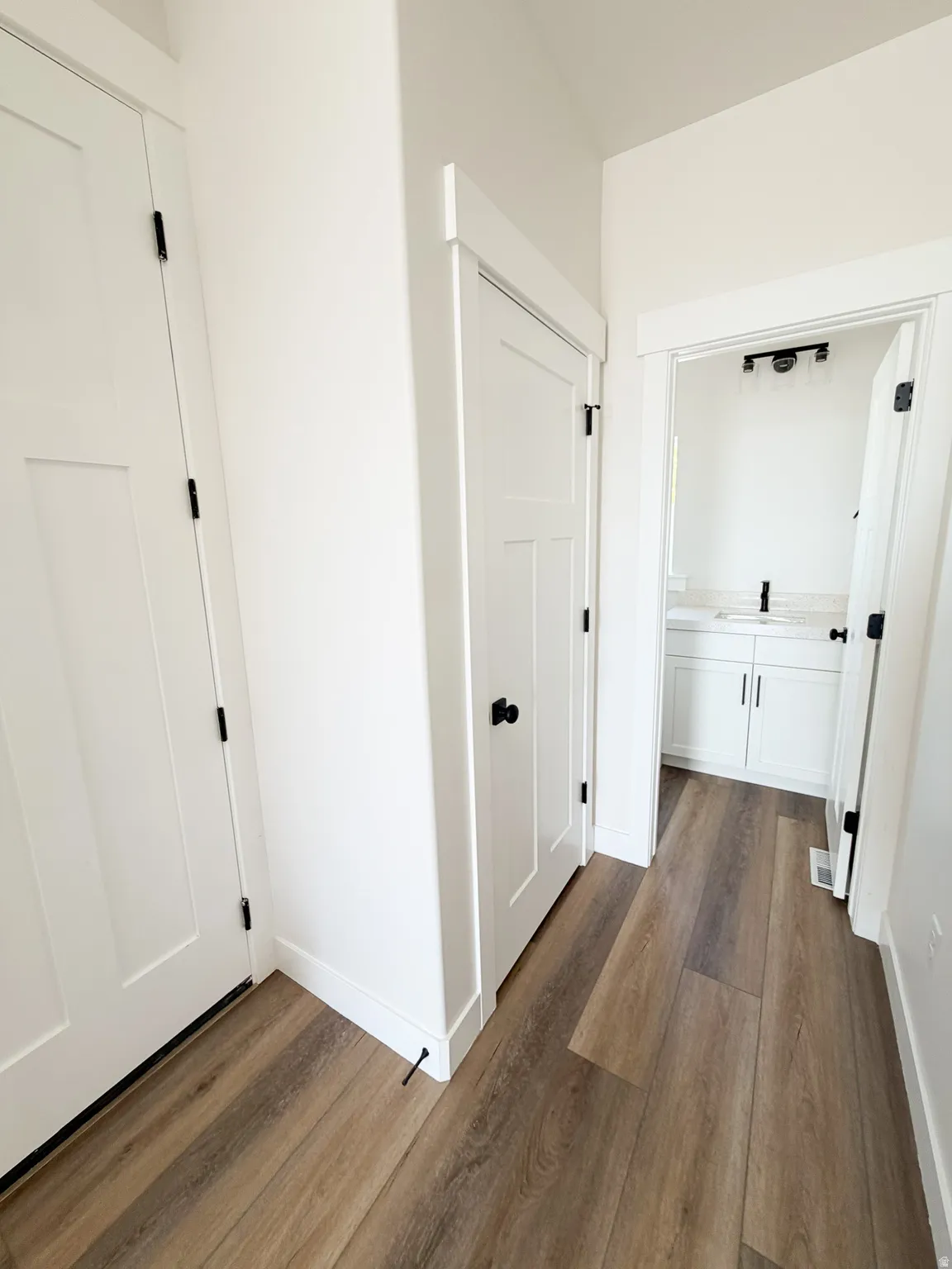 Hallway featuring wood-finish flooring, white paneled doors with black hardware, and crisp white baseboards