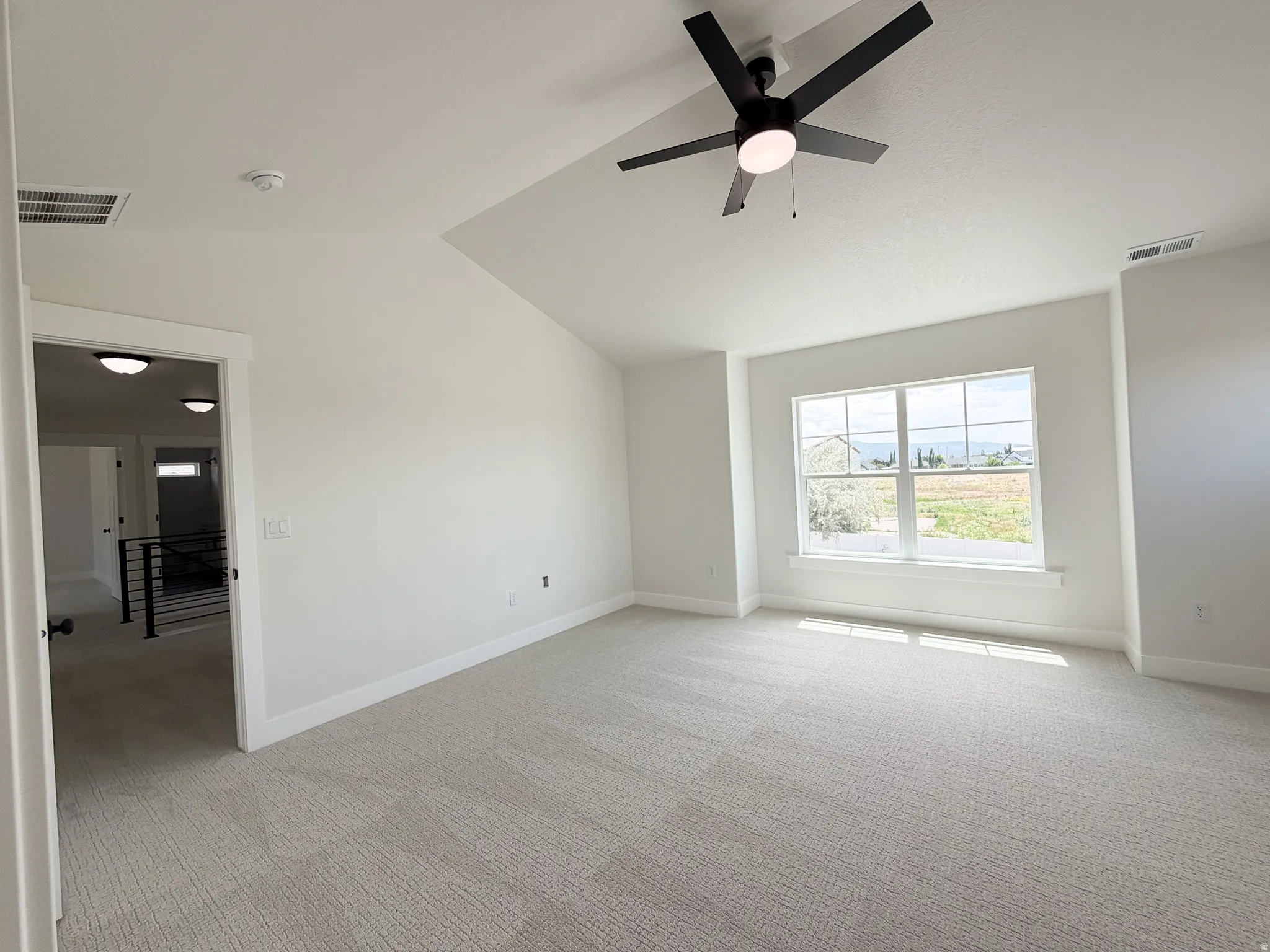 Spacious room with light-toned patterned carpet, a vaulted ceiling, and a contemporary ceiling fan