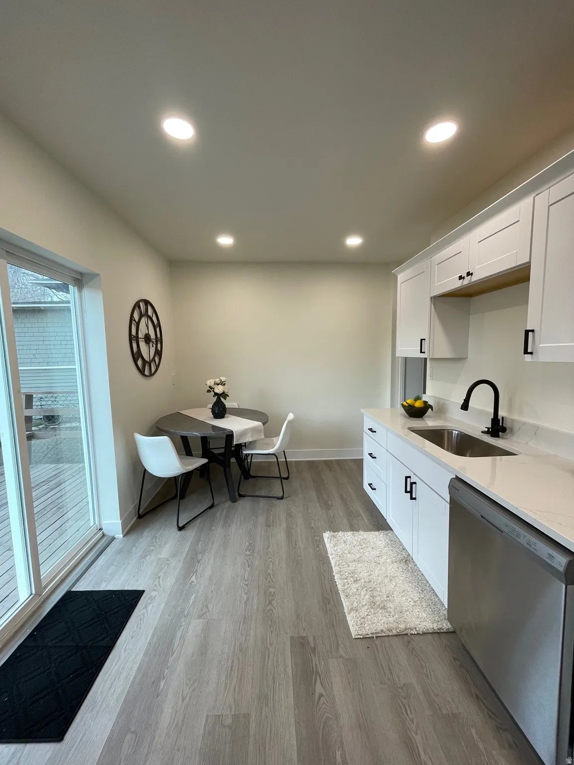 Kitchen featuring white cabinets, dishwasher, light wood-style floors, light stone counters, and recessed lighting