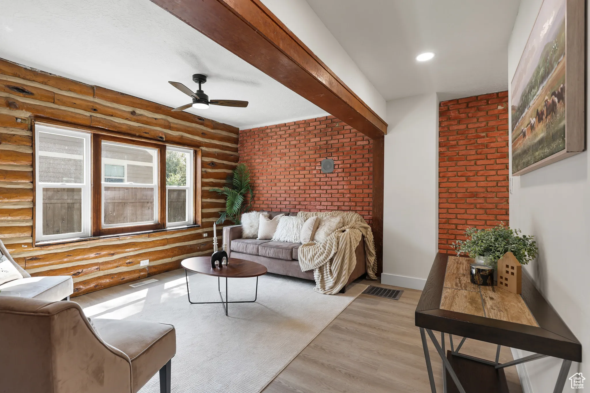 Living room featuring wood finished floors, a ceiling fan, brick wall, and beam ceiling