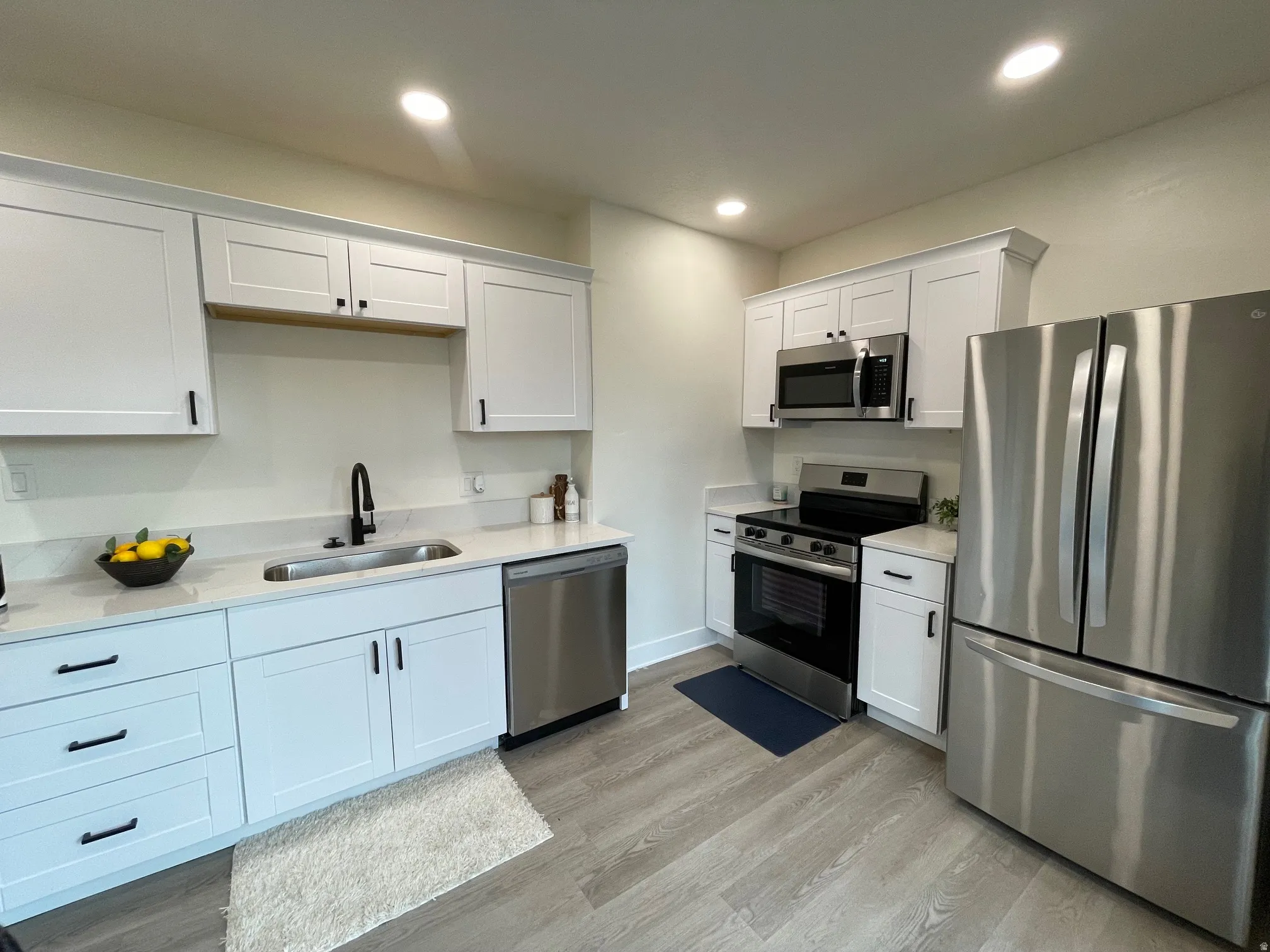 Kitchen featuring stainless steel appliances, white cabinetry, light wood-type flooring, light stone counters, and recessed lighting