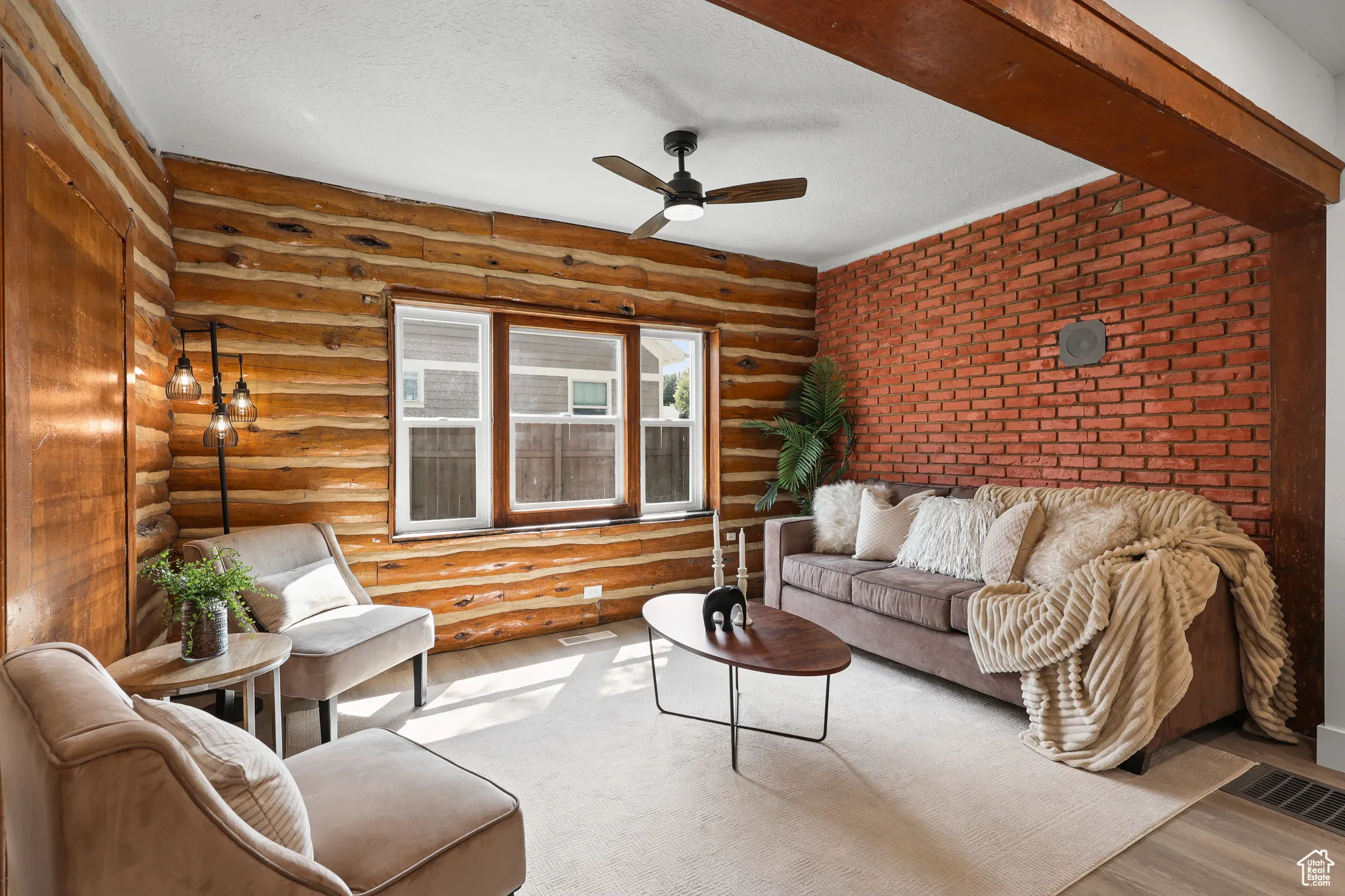 Living area featuring a ceiling fan, a textured ceiling, wood finished floors, rustic walls, and brick wall