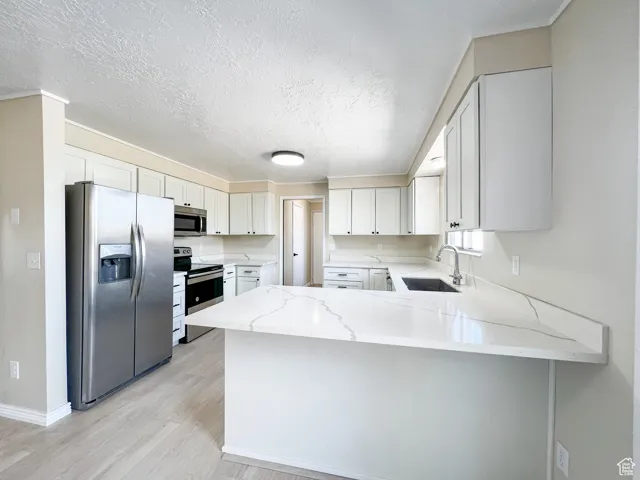 Kitchen with stainless steel appliances, a peninsula, light stone countertops, light wood-style floors, and white cabinets