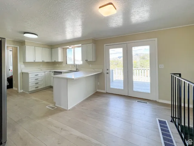 Kitchen featuring a peninsula, light countertops, a textured ceiling, light wood-type flooring, and white cabinetry
