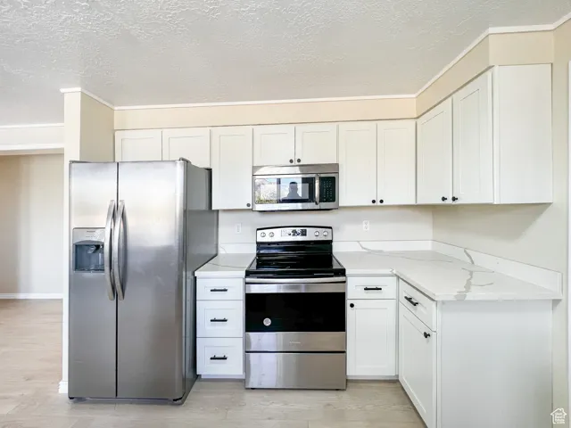 Kitchen featuring appliances with stainless steel finishes, light wood-type flooring, ornamental molding, light stone counters, and white cabinets