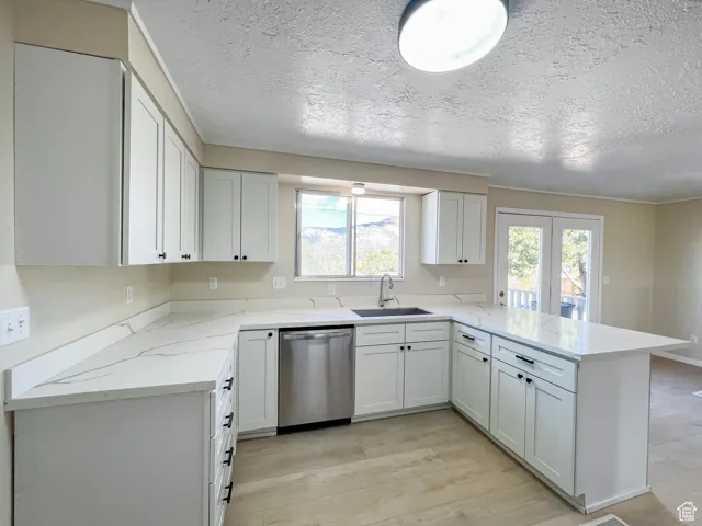 Kitchen featuring a peninsula, light wood-type flooring, stainless steel dishwasher, a textured ceiling, and light stone countertops
