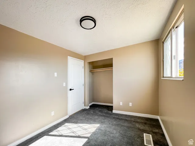 Unfurnished bedroom featuring a textured ceiling, dark carpet, and a closet