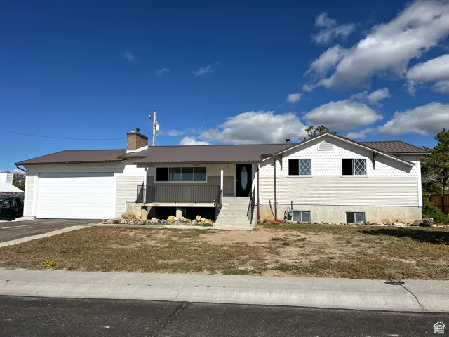 Ranch-style house featuring covered porch, a metal roof, a garage, a chimney, and asphalt driveway