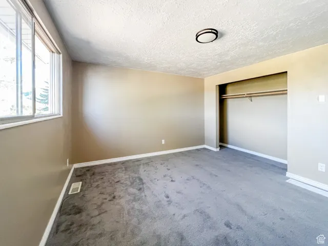 Unfurnished bedroom featuring carpet flooring, a textured ceiling, and a closet