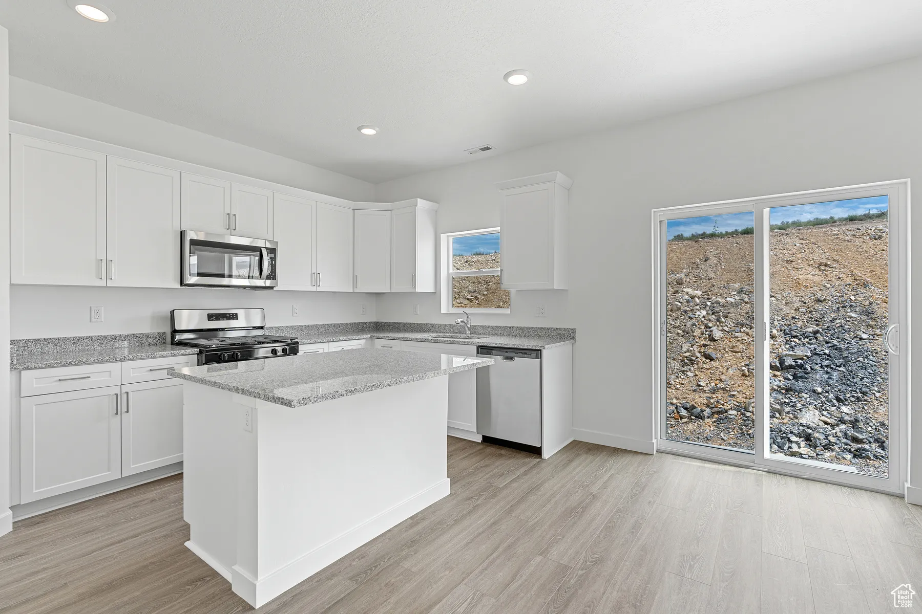 Kitchen featuring stainless steel appliances, white cabinetry, a kitchen island, recessed lighting, and light wood-style floors