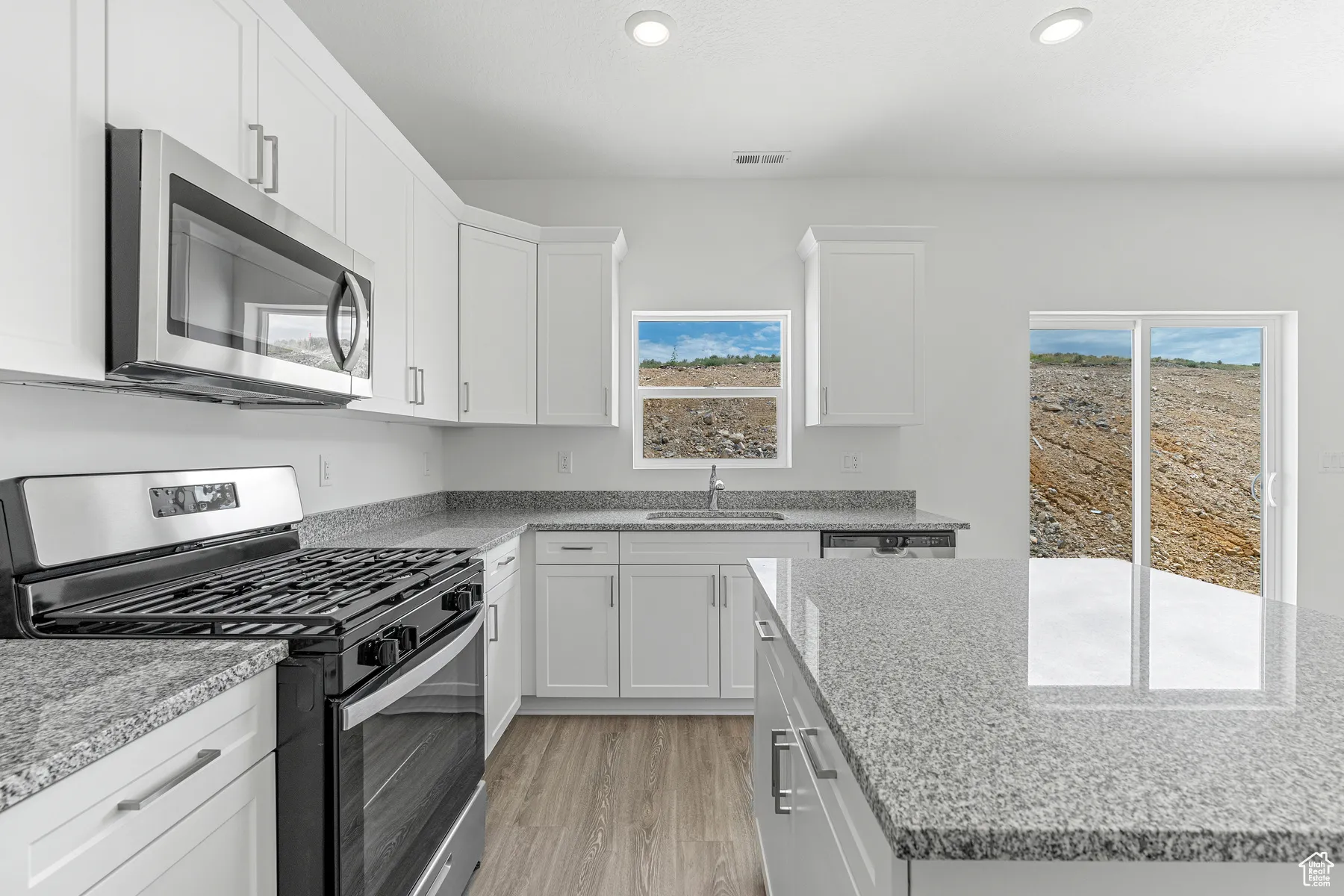 Kitchen featuring stainless steel appliances, light wood finished floors, white cabinetry, light stone counters, and recessed lighting