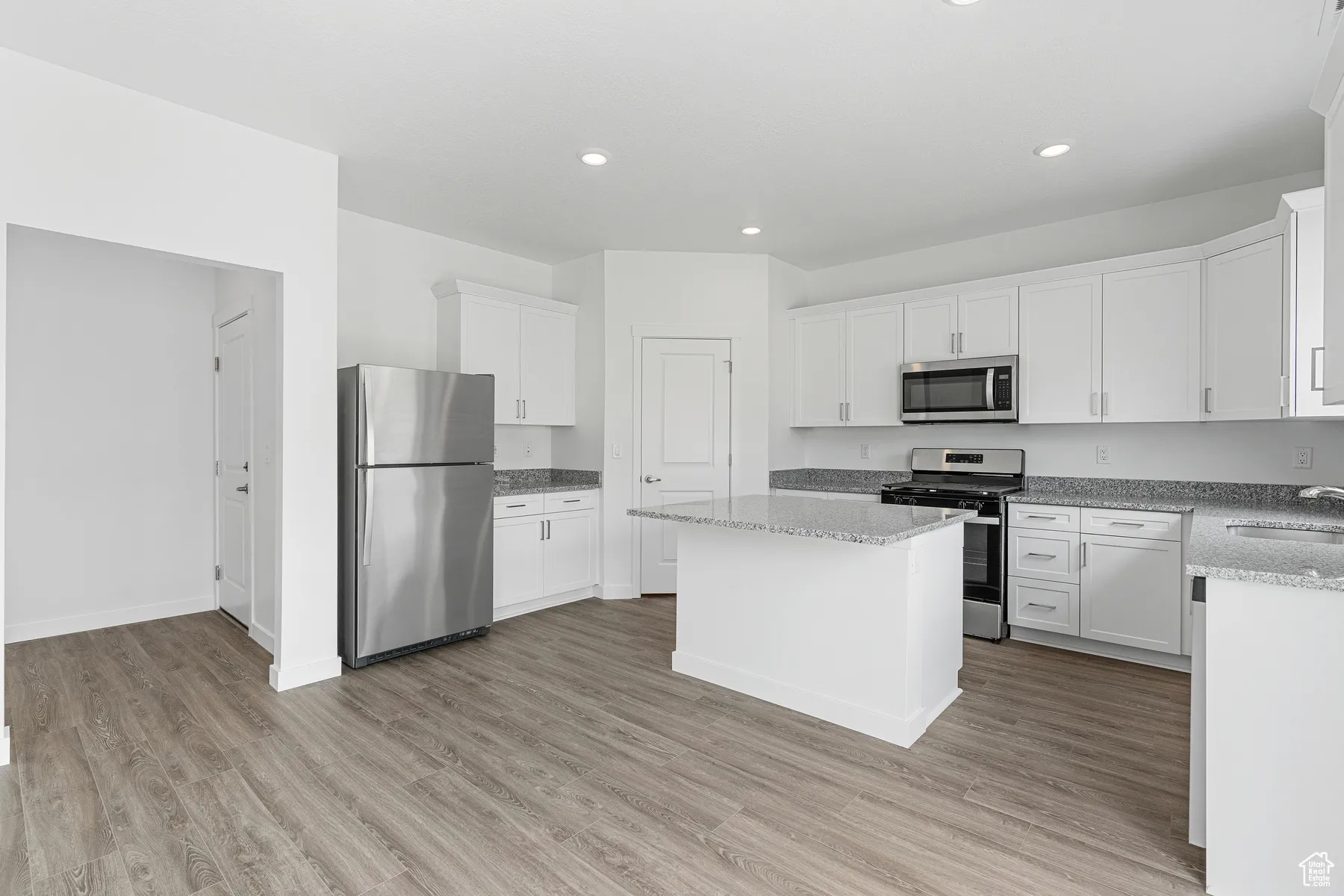 Kitchen with appliances with stainless steel finishes, a kitchen island, light wood-style flooring, white cabinetry, and recessed lighting