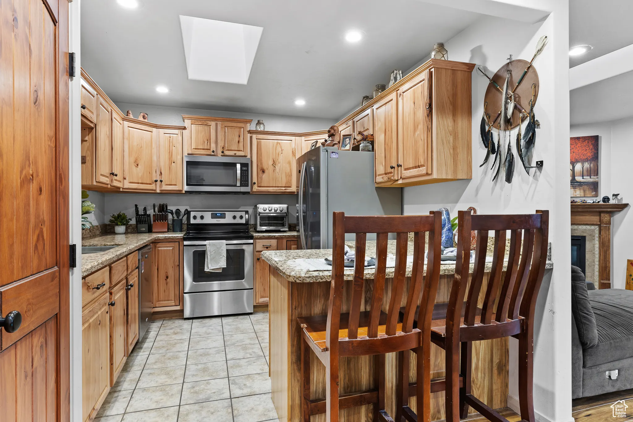 Kitchen featuring stainless steel appliances, recessed lighting, light tile patterned floors, light stone counters, and a skylight
