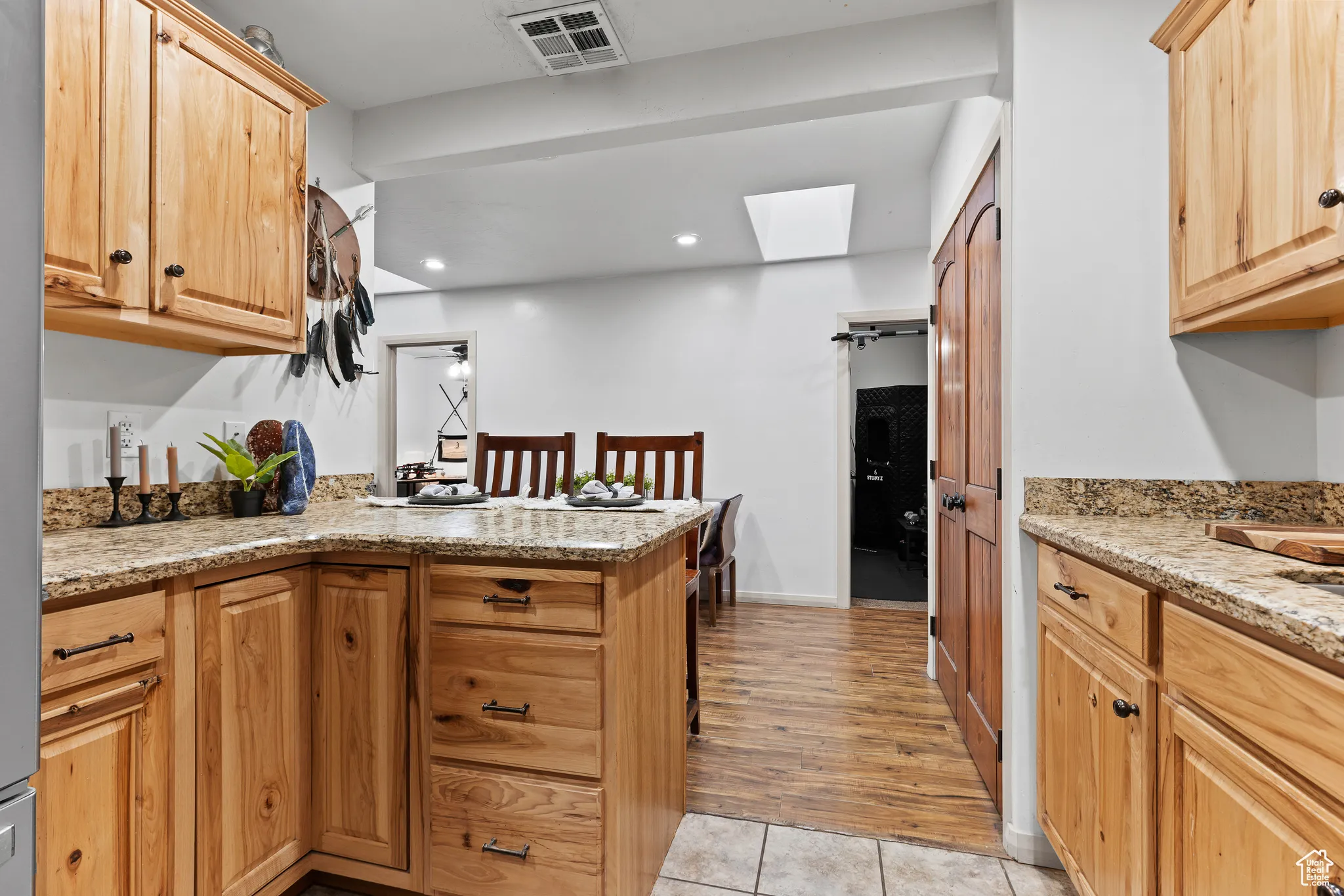 Kitchen featuring a skylight, light brown cabinets, recessed lighting, a peninsula, and light stone counters