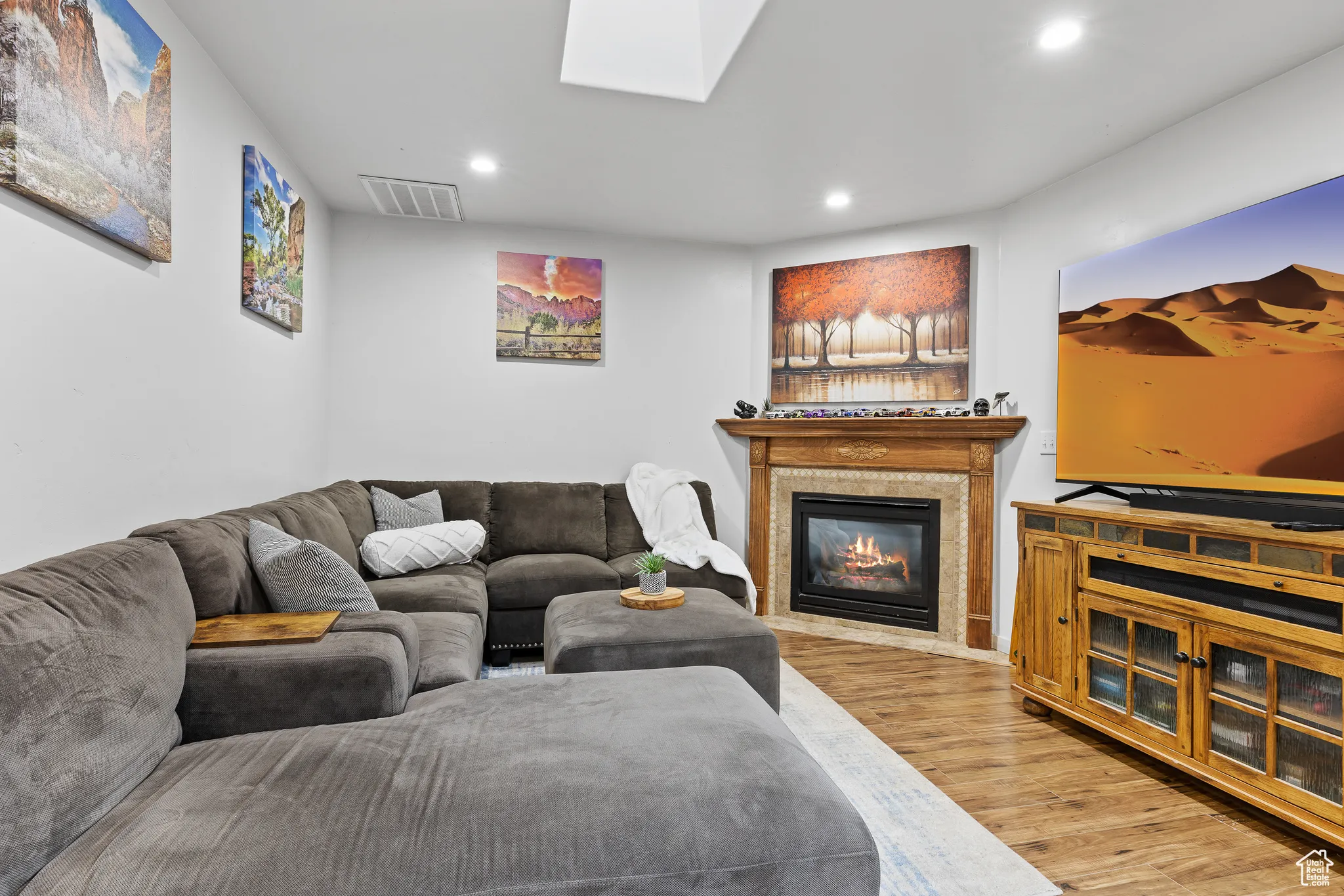Living room with wood finished floors, recessed lighting, a glass covered fireplace, and a skylight