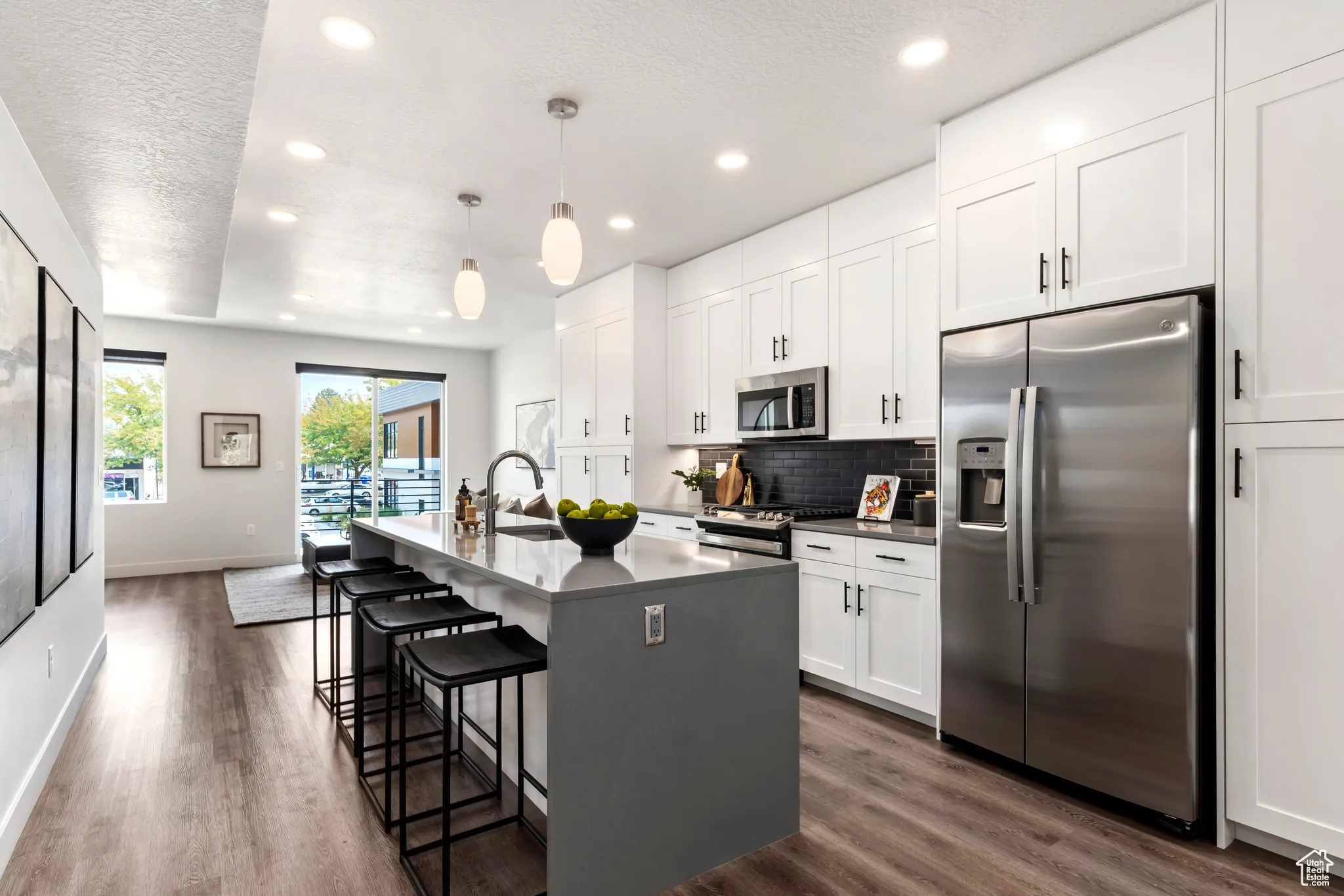 Kitchen featuring decorative backsplash, stainless steel appliances, a textured ceiling, dark wood finished floors, and white cabinetry
