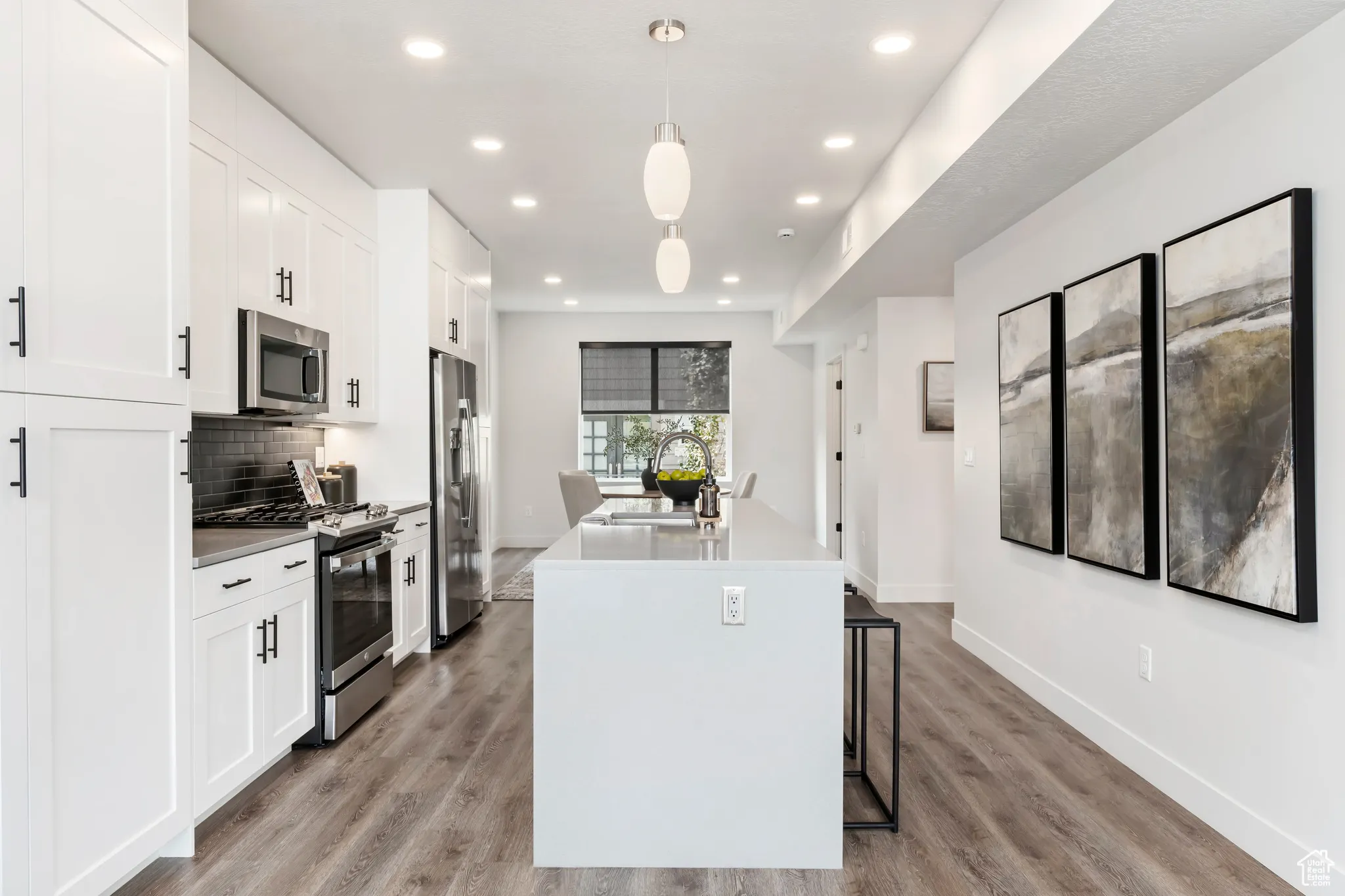 Kitchen featuring appliances with stainless steel finishes, a center island with sink, white cabinetry, light wood-style floors, and recessed lighting