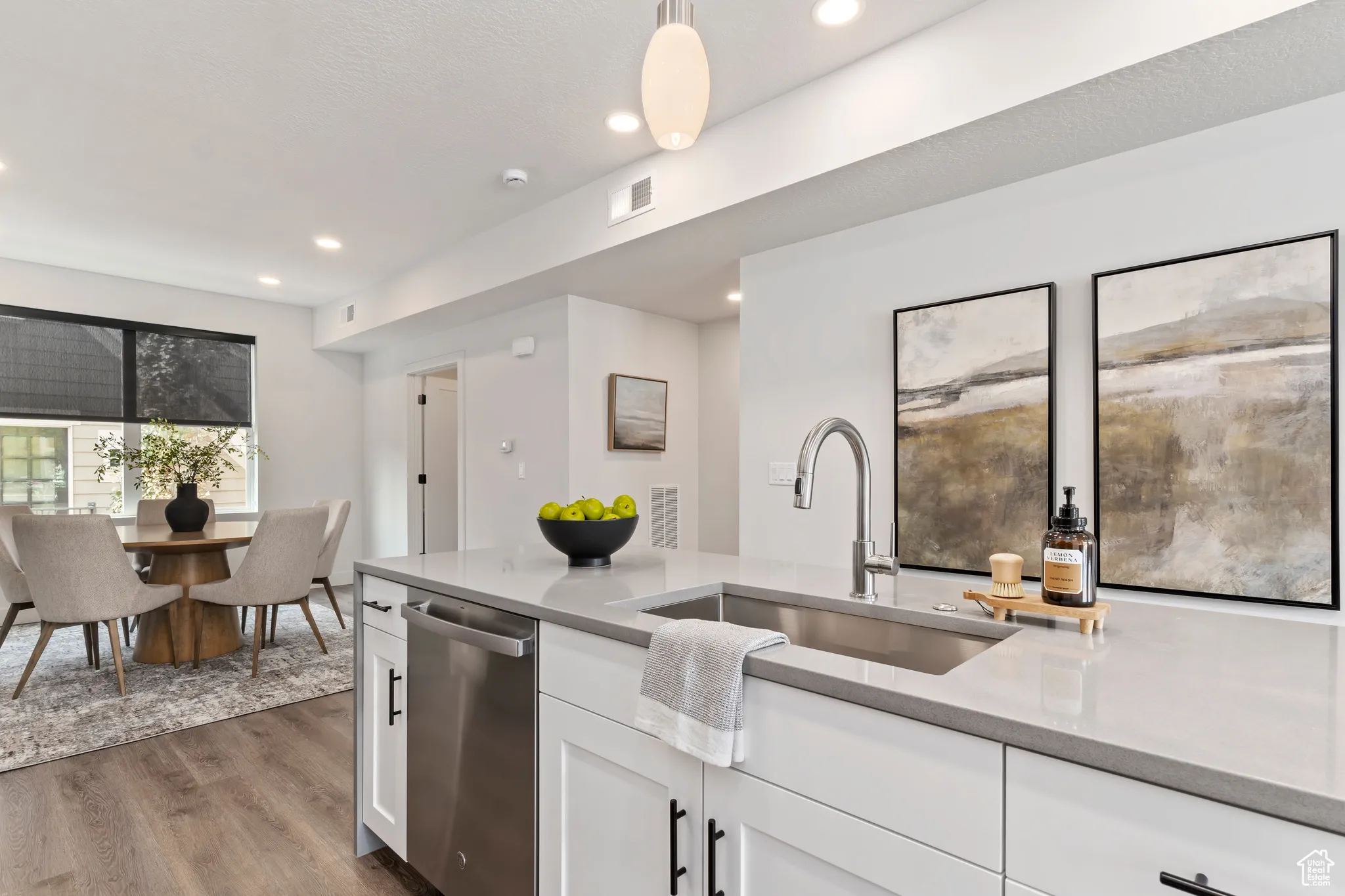 Kitchen with stainless steel dishwasher, white cabinets, dark wood-style floors, and recessed lighting