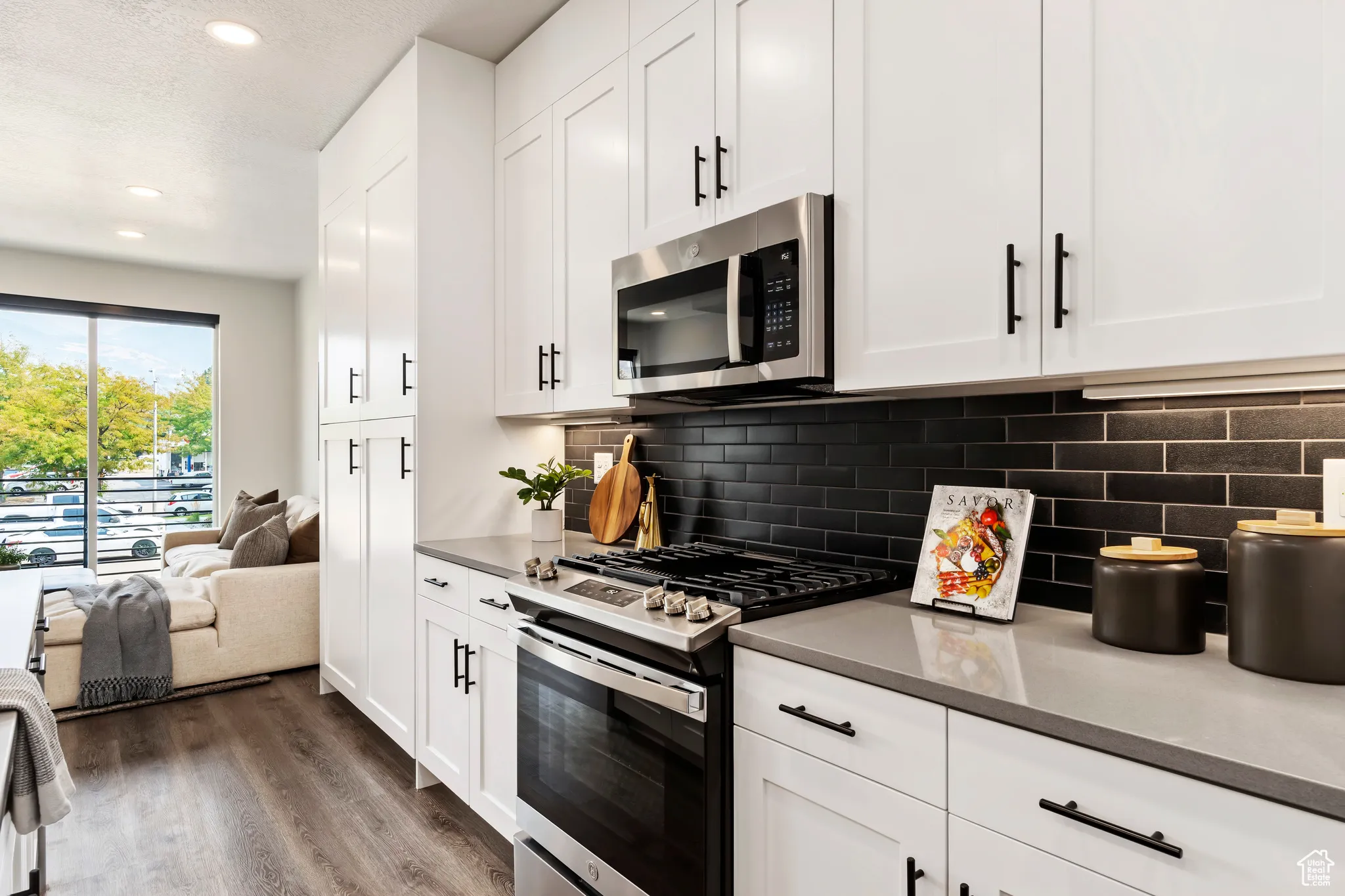 Kitchen with stainless steel appliances, dark wood-type flooring, white cabinets, recessed lighting, and tasteful backsplash