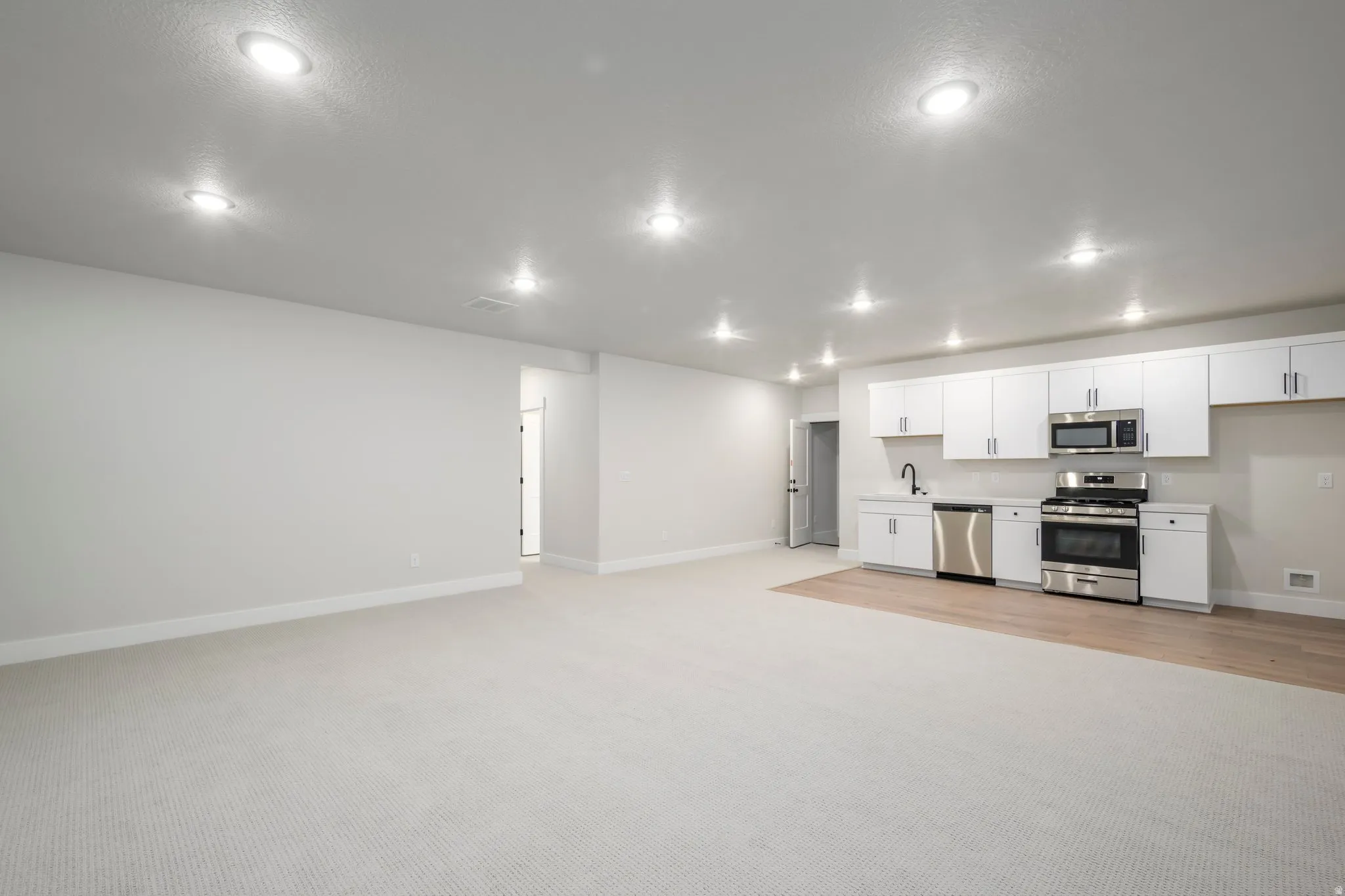Kitchen featuring stainless steel appliances, white cabinetry, open floor plan, light colored carpet, and light countertops
