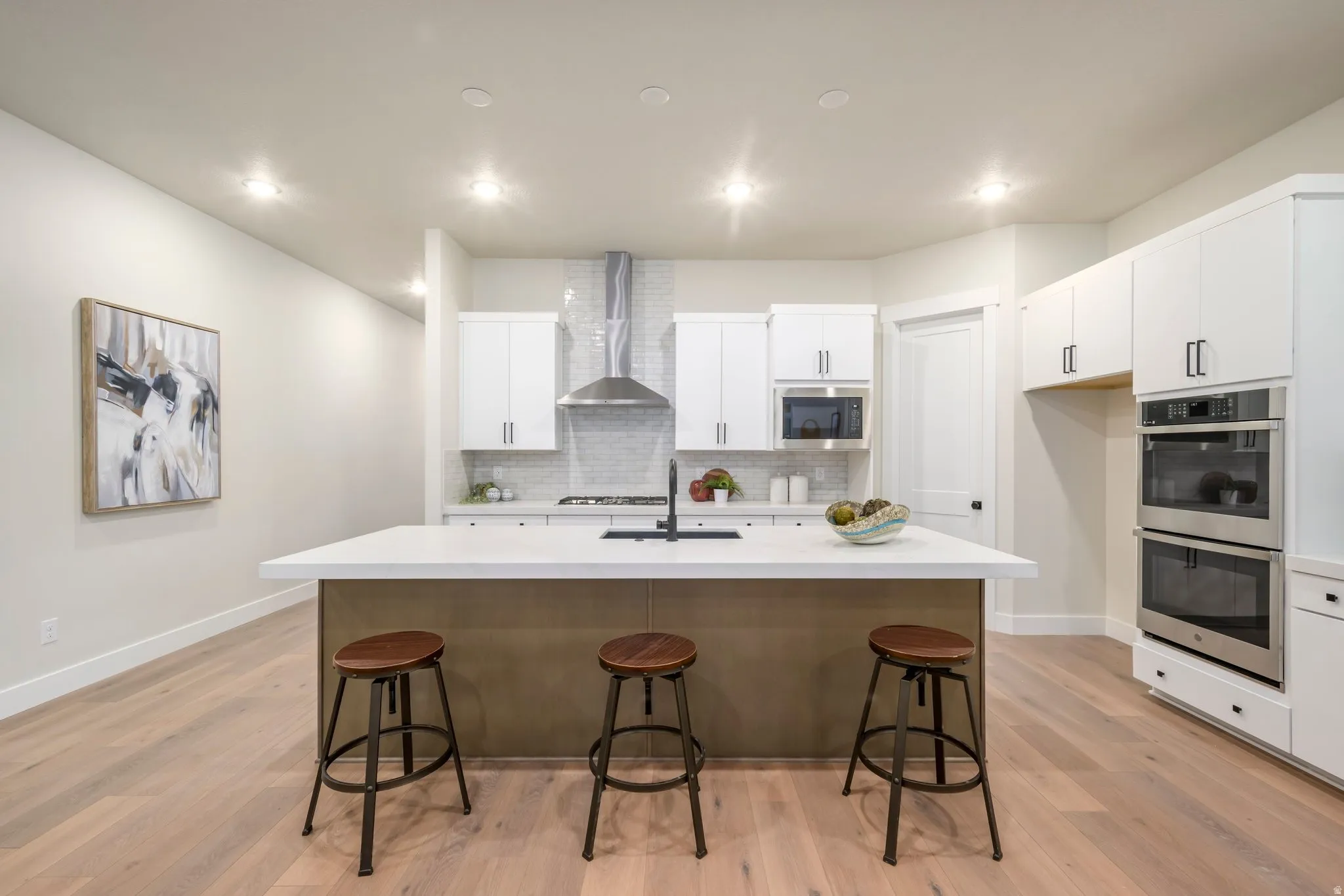 Kitchen featuring white cabinets, double oven, a kitchen breakfast bar, light wood-type flooring, and recessed lighting