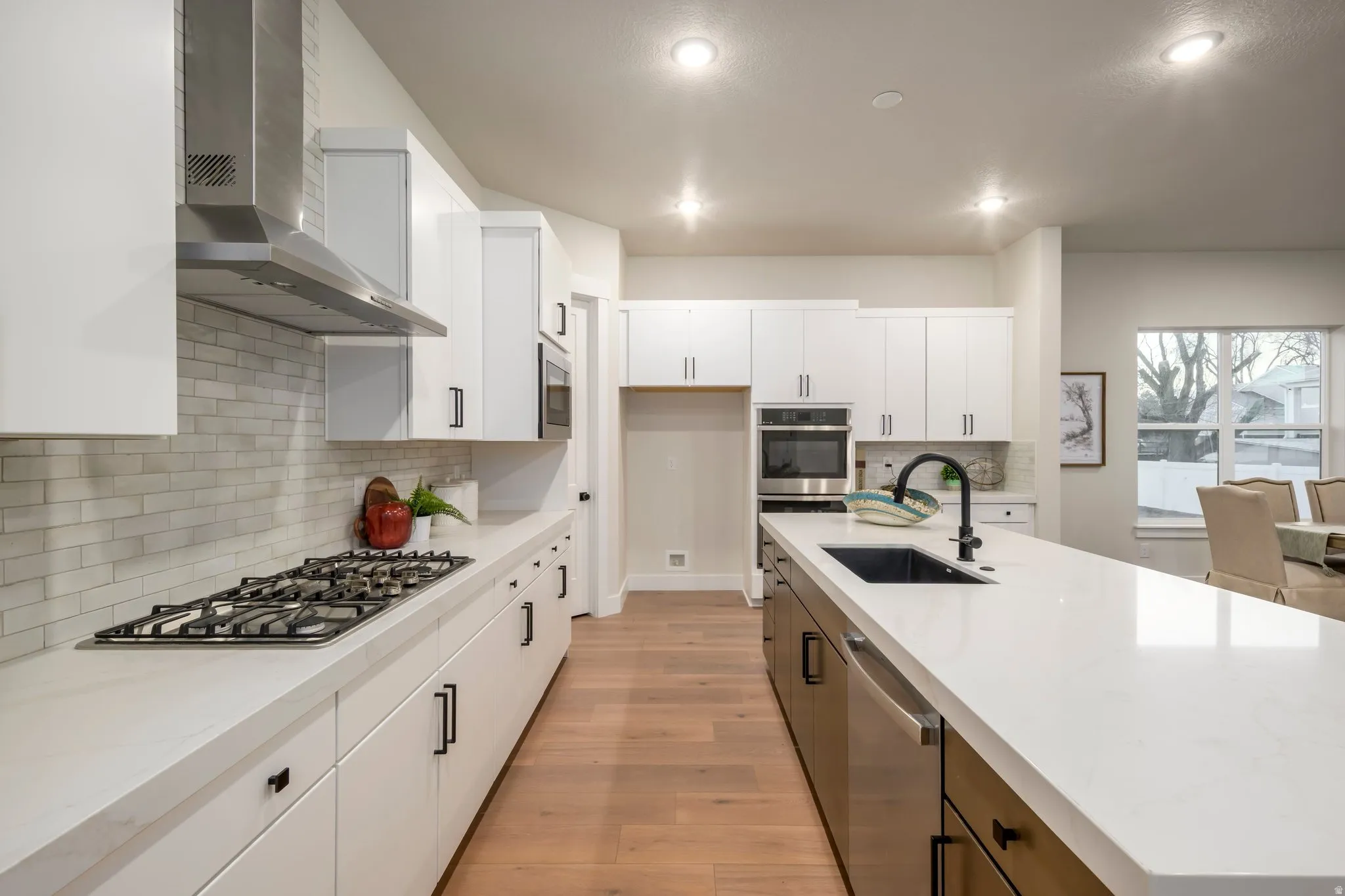 Kitchen featuring light wood-style flooring, dual tone cabinetry, stainless steel appliances, light stone countertops, and an island with sink