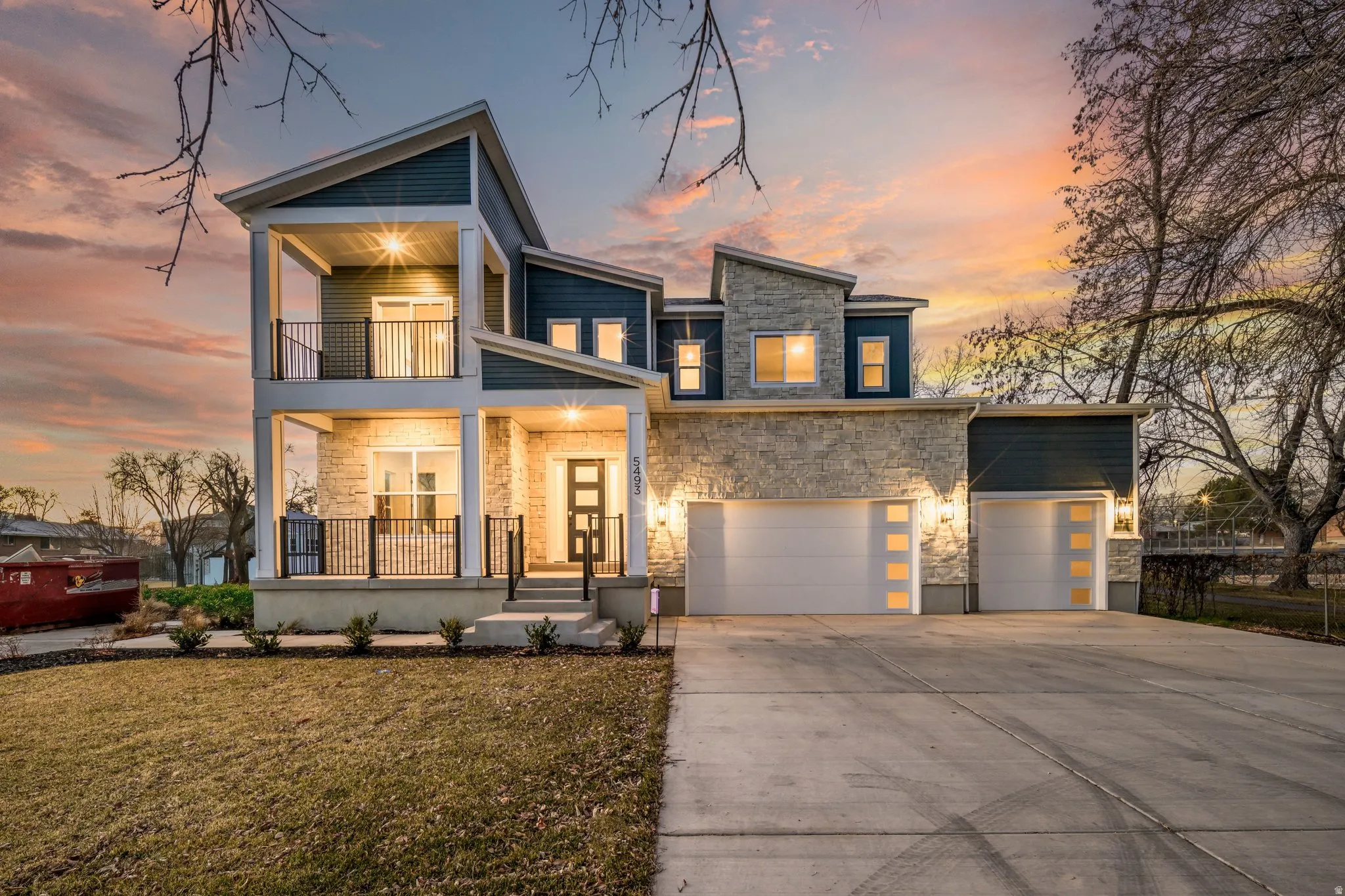 Modern home featuring stone siding, covered porch, driveway, a garage, and a lawn