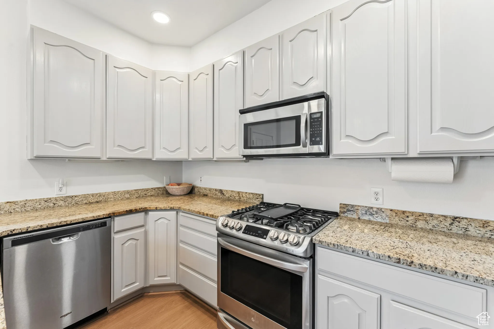 Kitchen featuring stainless steel appliances, light wood-style flooring, light stone counters, white cabinets, and recessed lighting