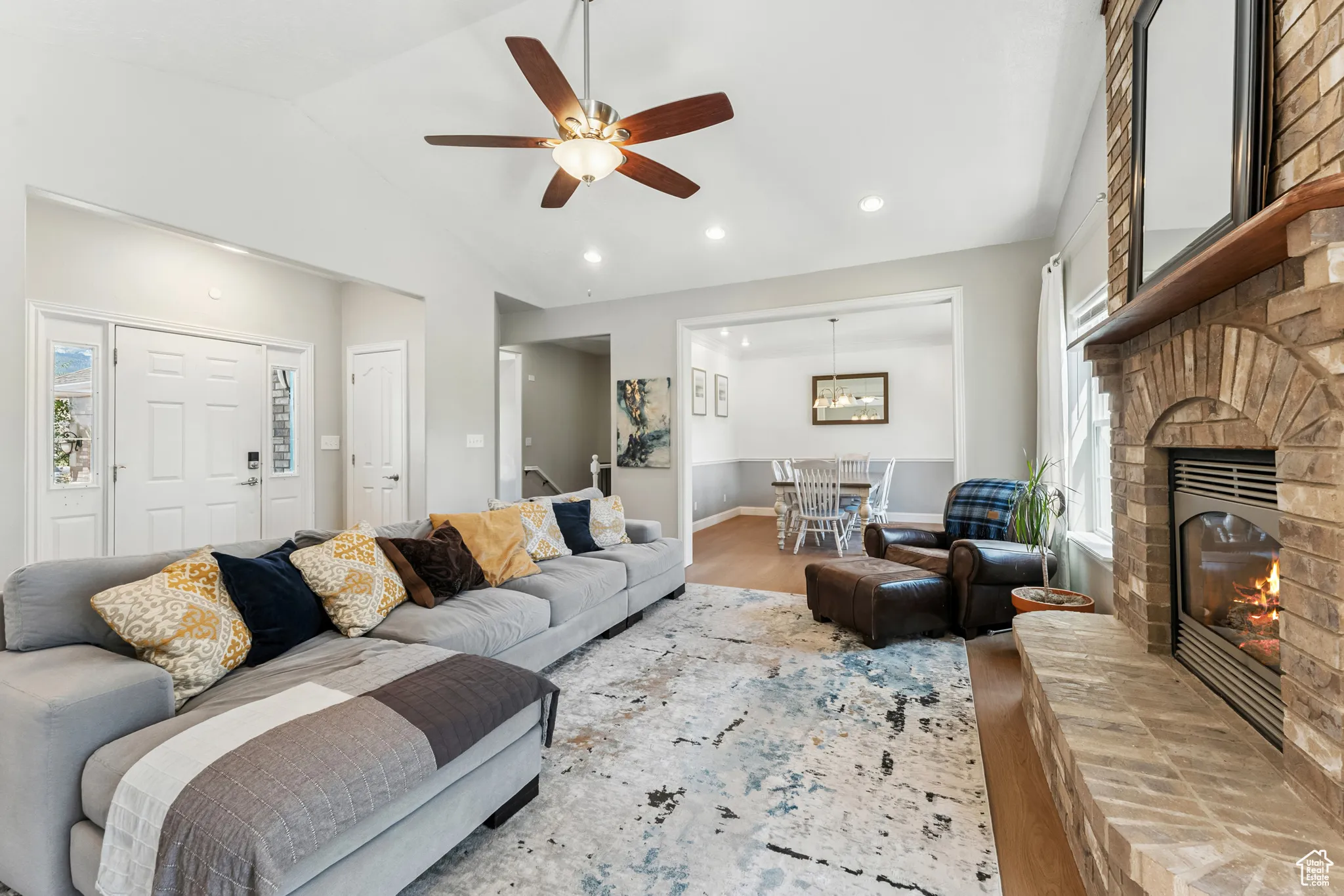 Living room featuring wood finished floors, lofted ceiling, a ceiling fan, recessed lighting, and a brick fireplace
